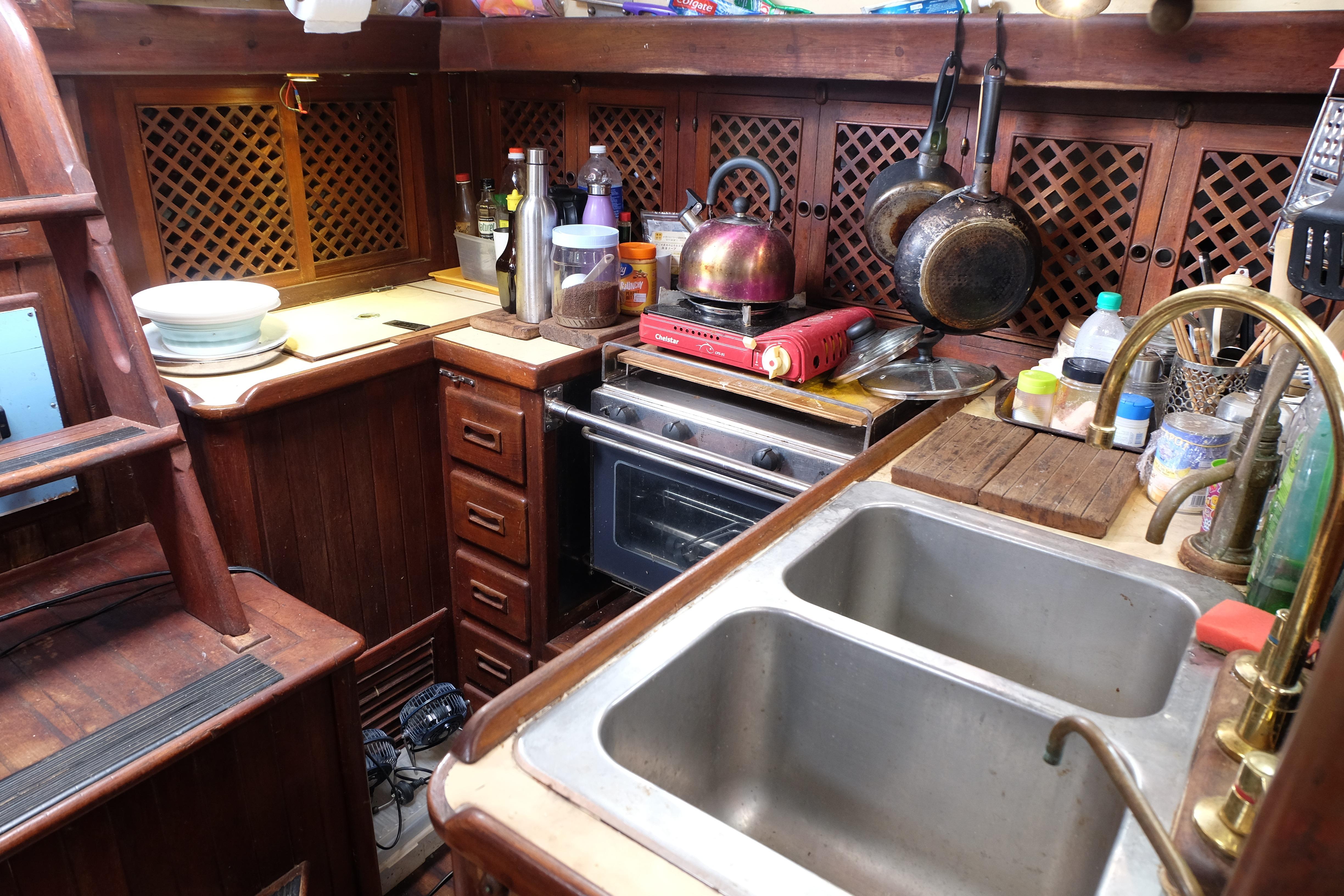 Cozy 1979 Westwind 35 yacht kitchen with wooden cabinetry, stove, and double sink.