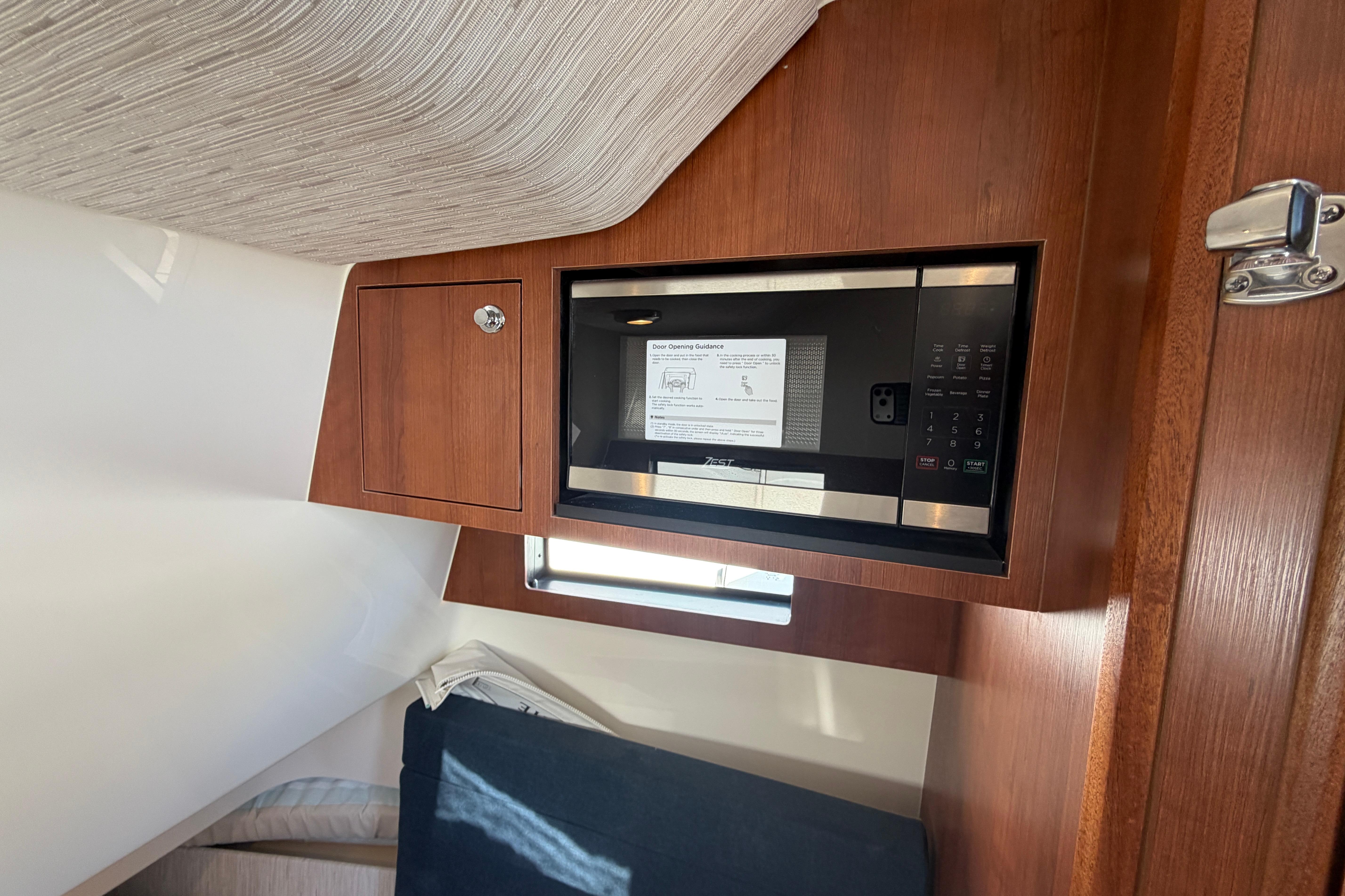 Interior of 2026 Pursuit S 358 Sport boat featuring a built-in microwave and wooden cabinetry.