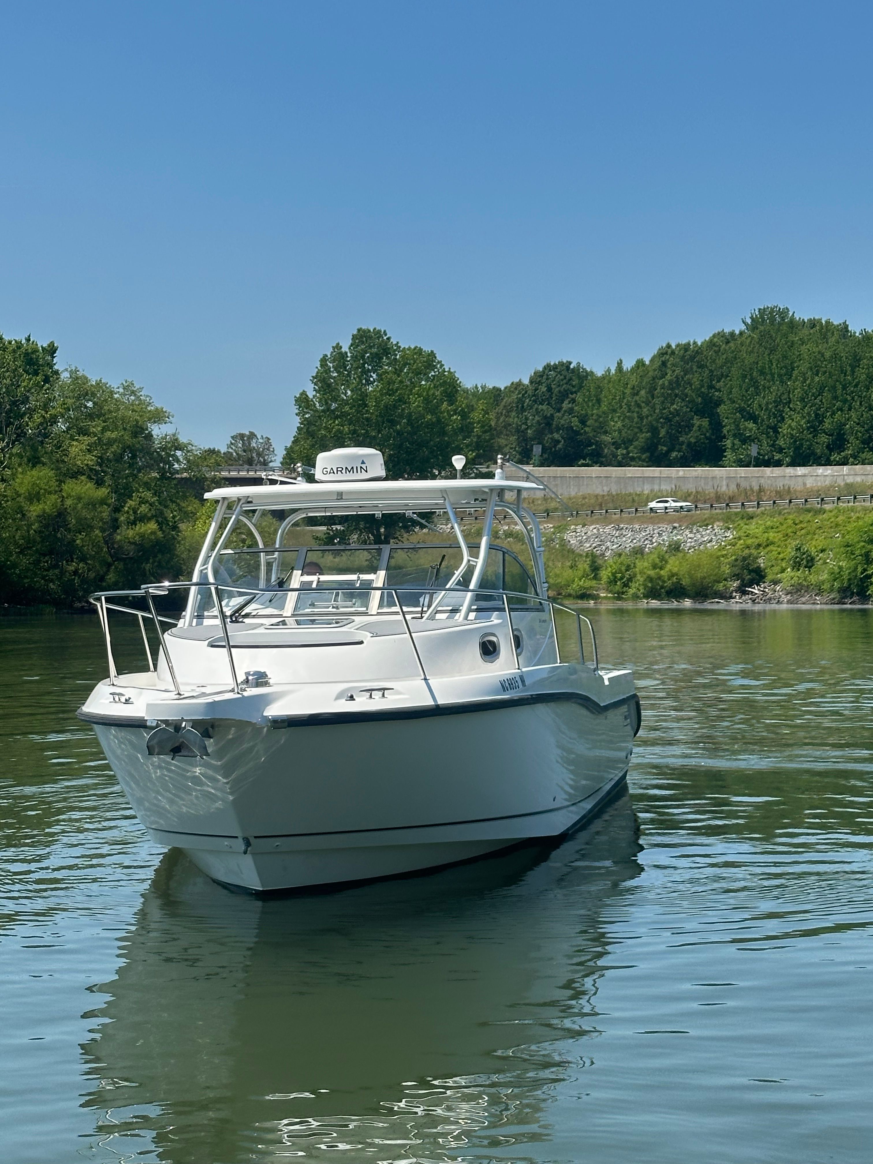 A 2006 Boston Whaler 305 Conquest on calm water, surrounded by trees and a road in the background.