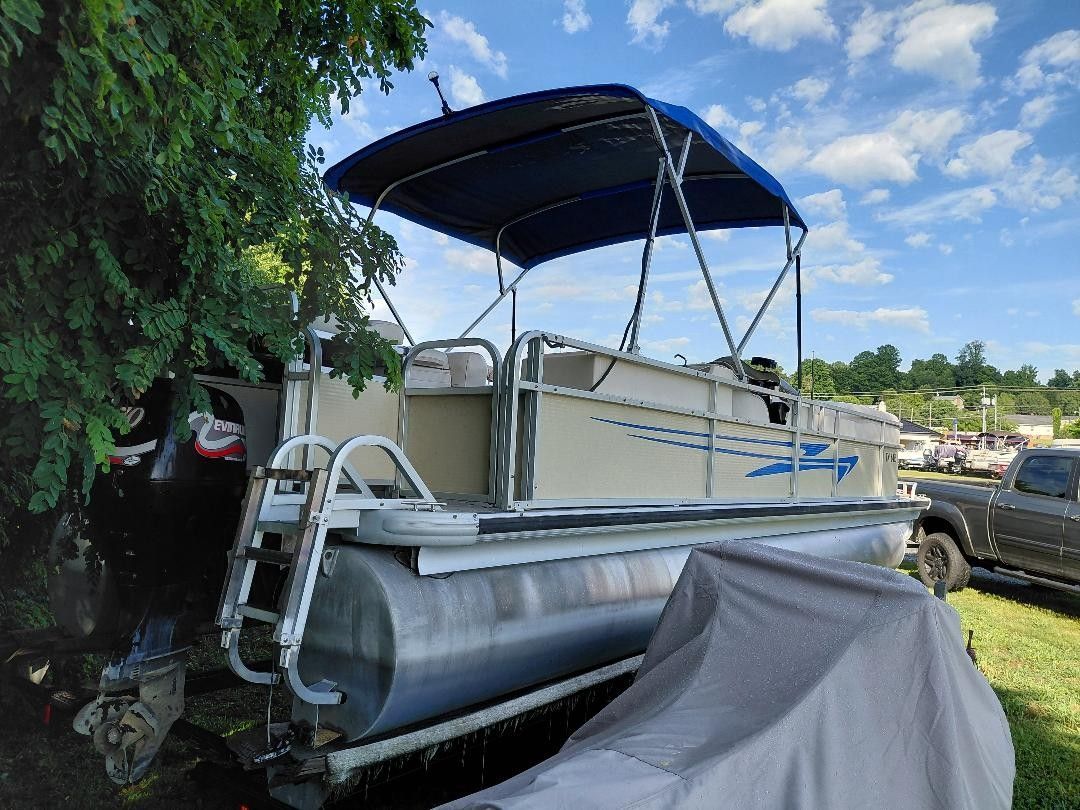 A 1999 Premier 250 Grand Majestic pontoon boat with a blue canopy, parked on a trailer.