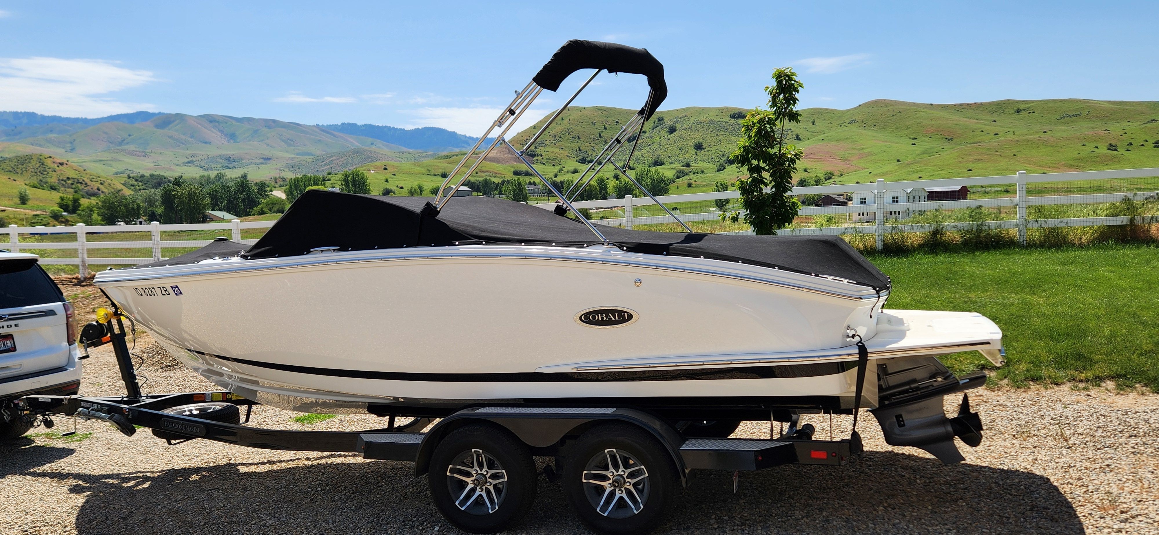 A white Cobalt CS22 boat on a trailer, surrounded by green hills and a blue sky.