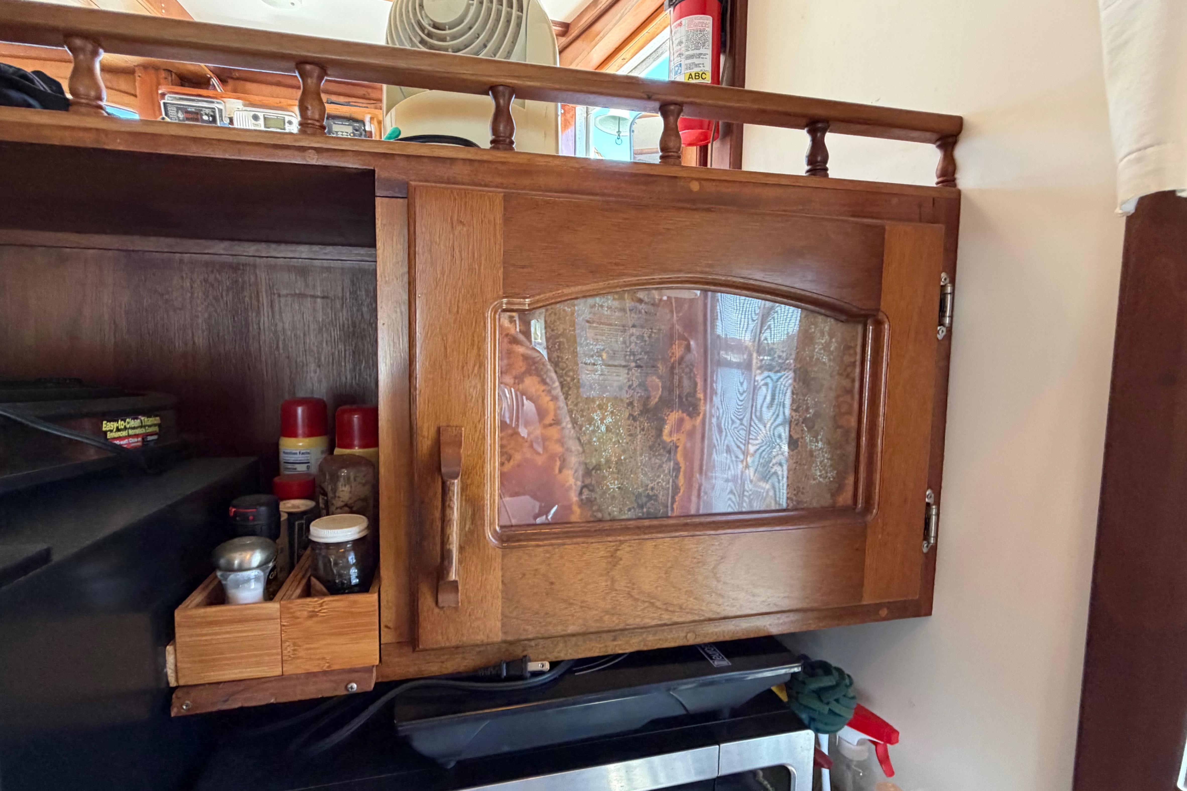Wooden cabinet with glass door on a 1985 Gozzard PILGRIM boat, containing spices and kitchen items.