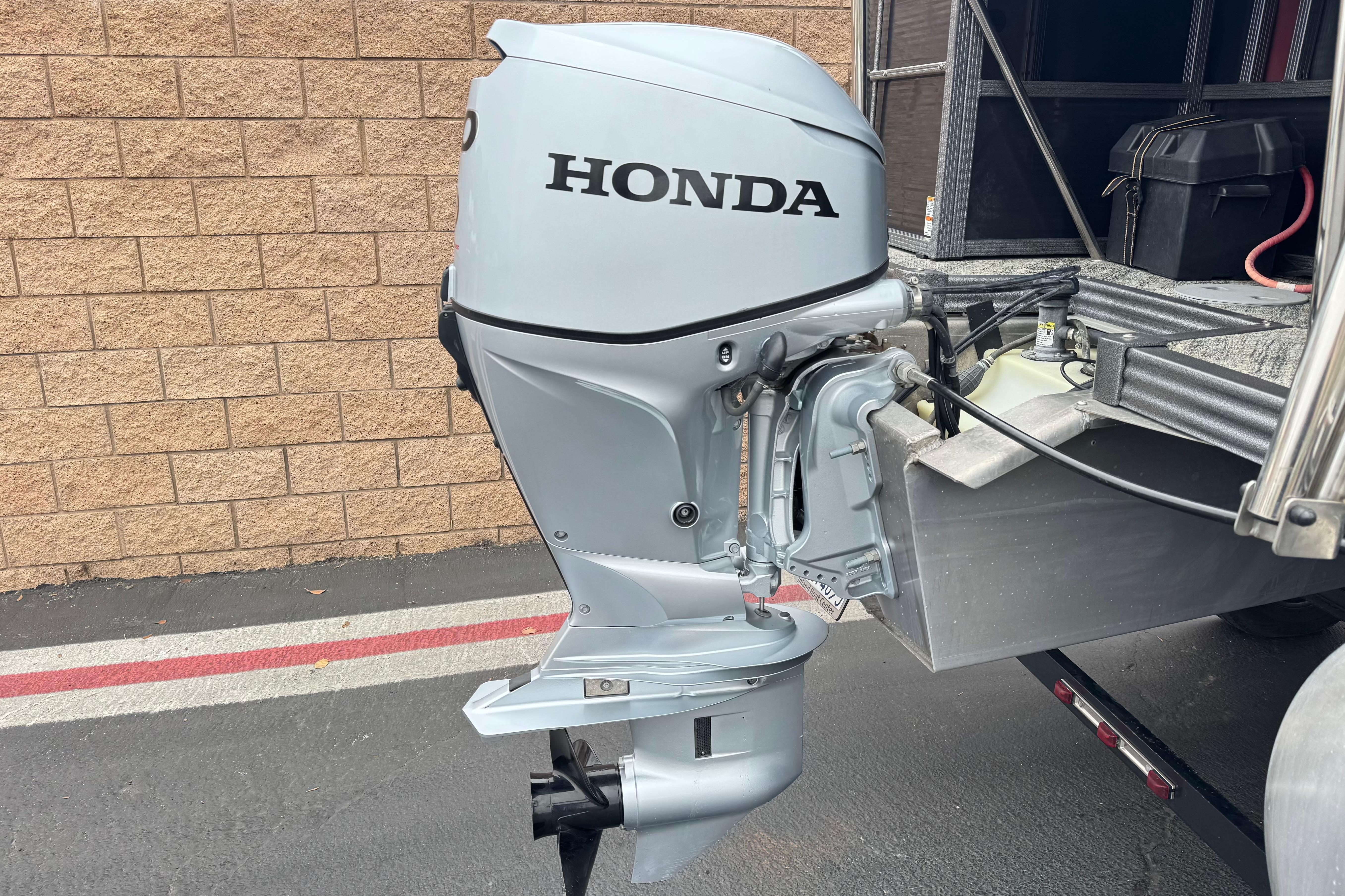 Honda outboard motor on 2020 Manitou 18 Aurora LE boat, parked by brick wall.
