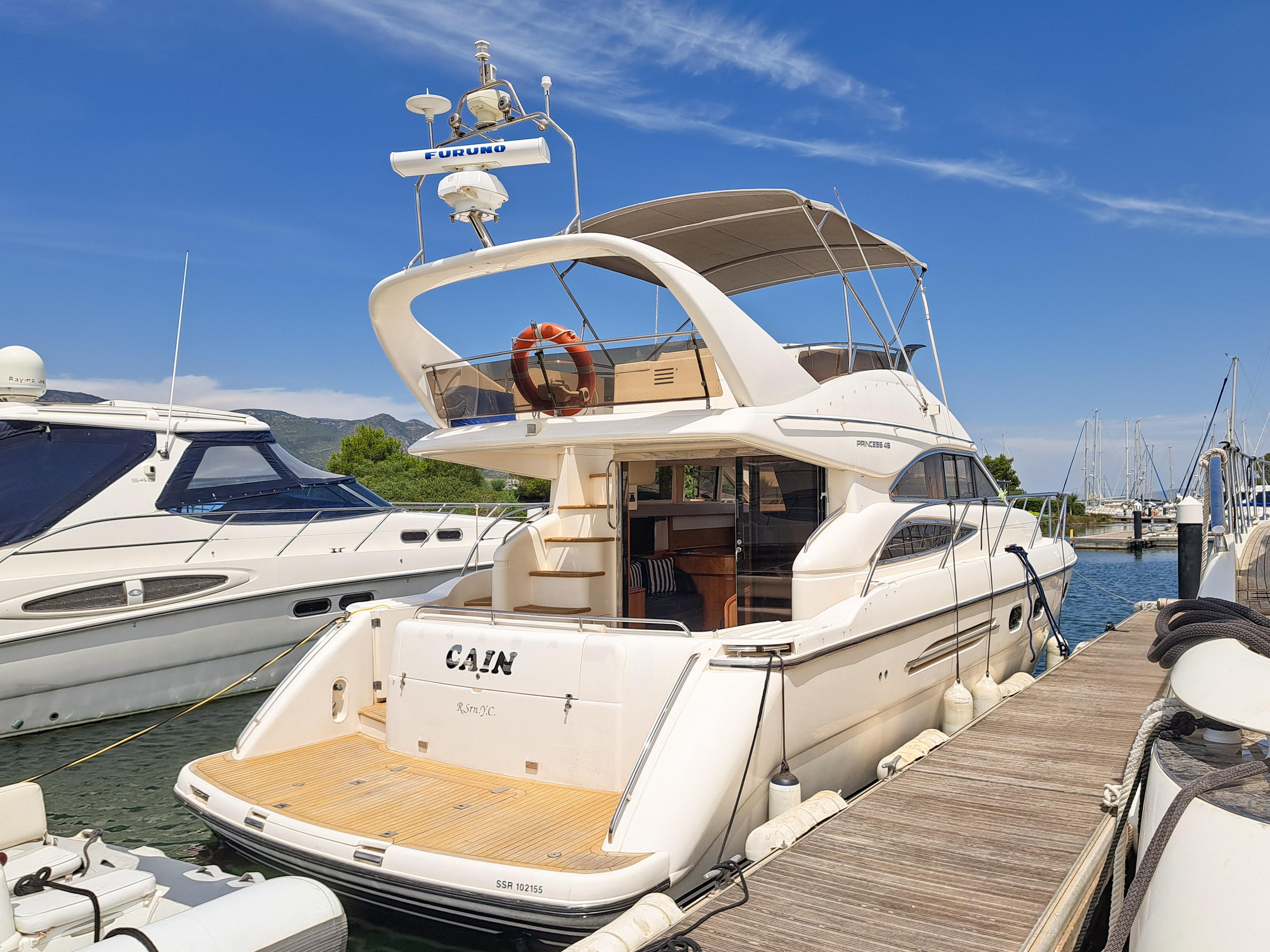 2002 Princess 45 Flybridge yacht docked at marina under clear blue sky.