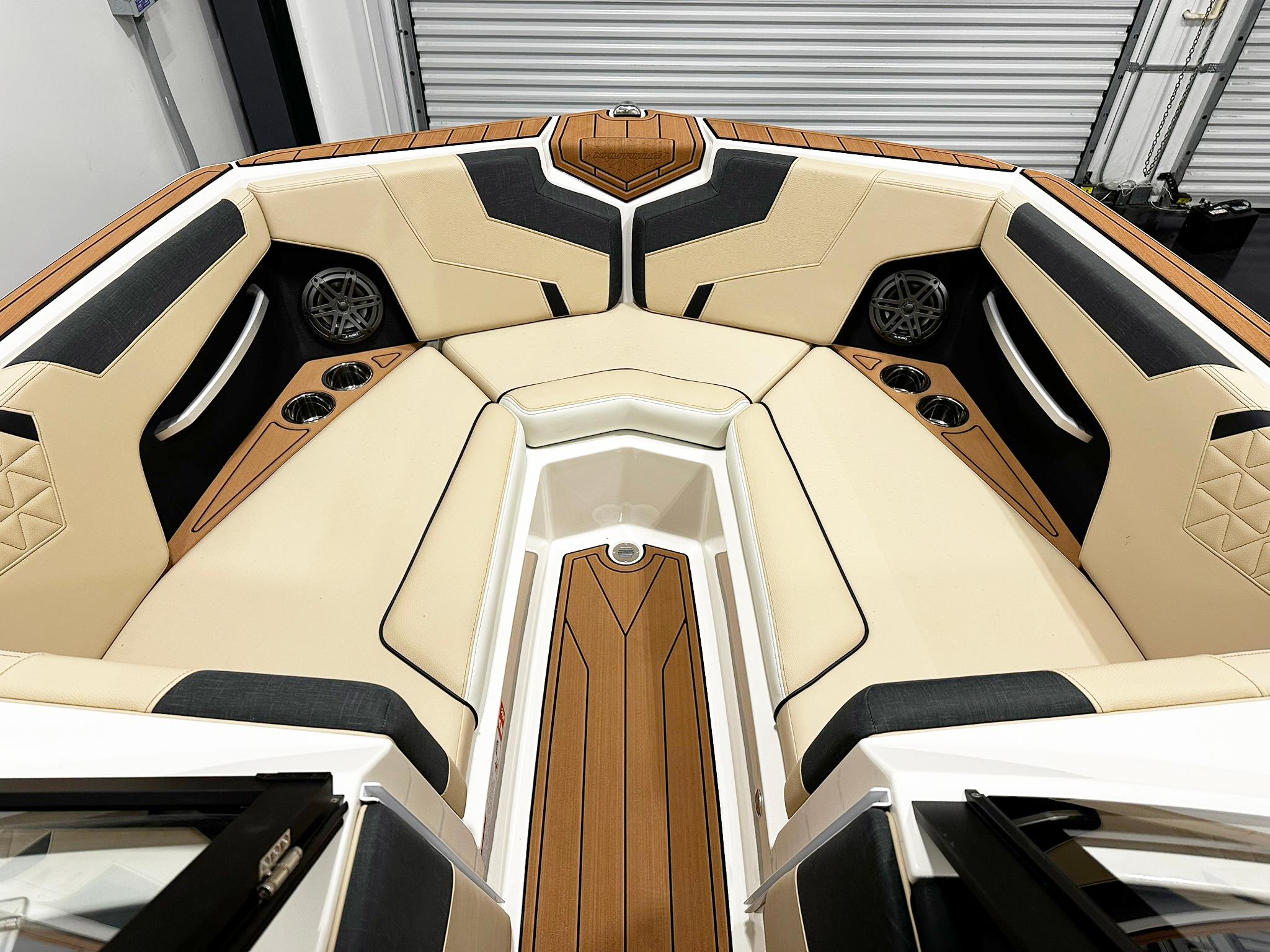2026 Nautique GS24 boat interior with beige and black seating, cup holders, and speakers.