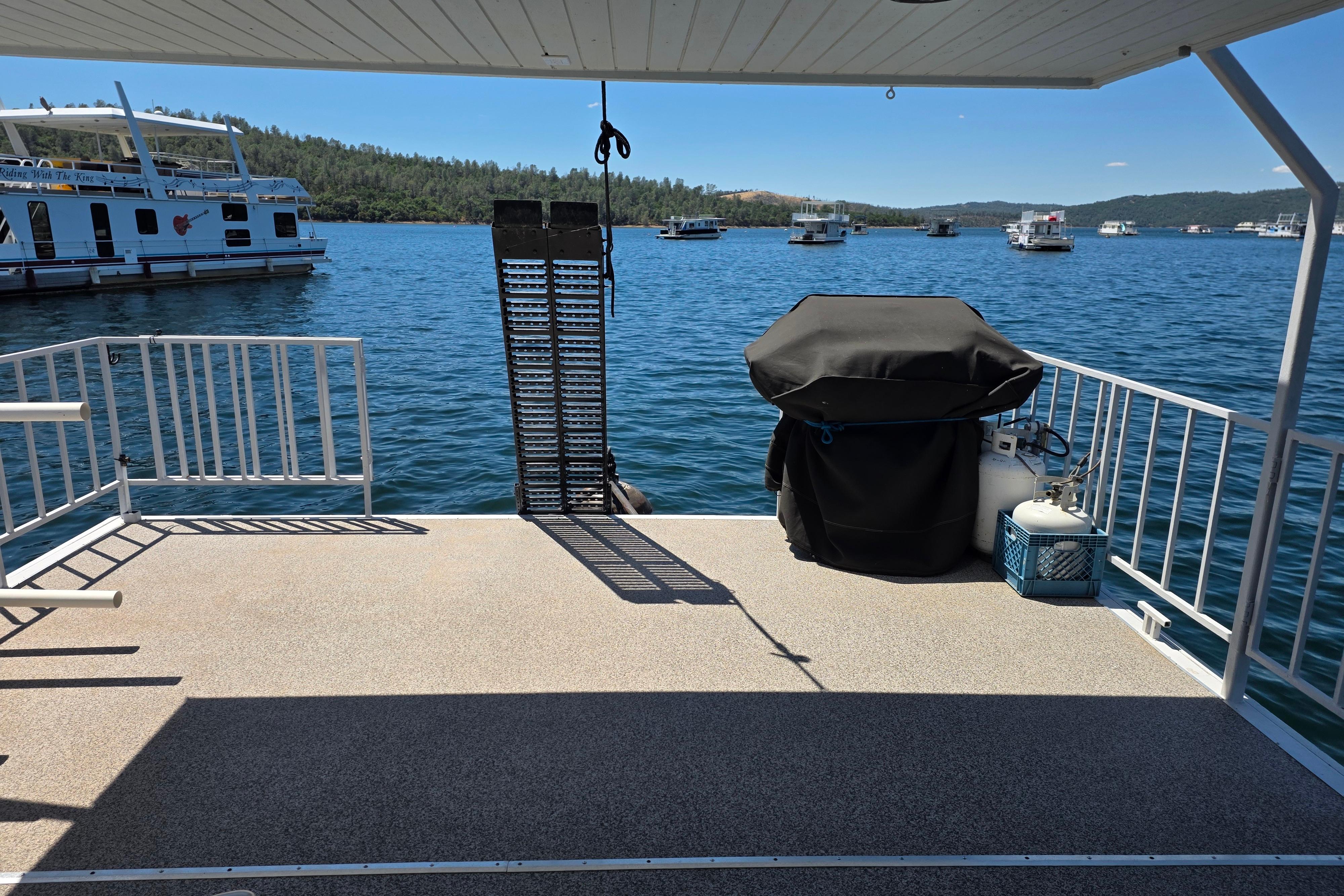 Houseboat deck with grill overlooking a scenic lake, surrounded by other boats.