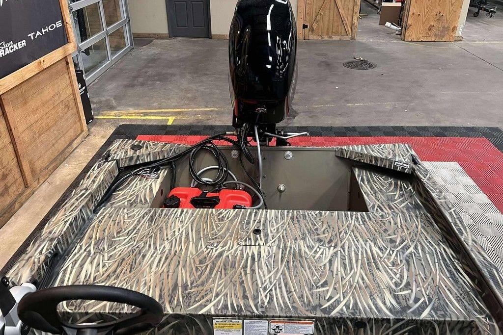 2026 Tracker Grizzly 1648 SC boat with camouflage design and outboard motor in showroom.