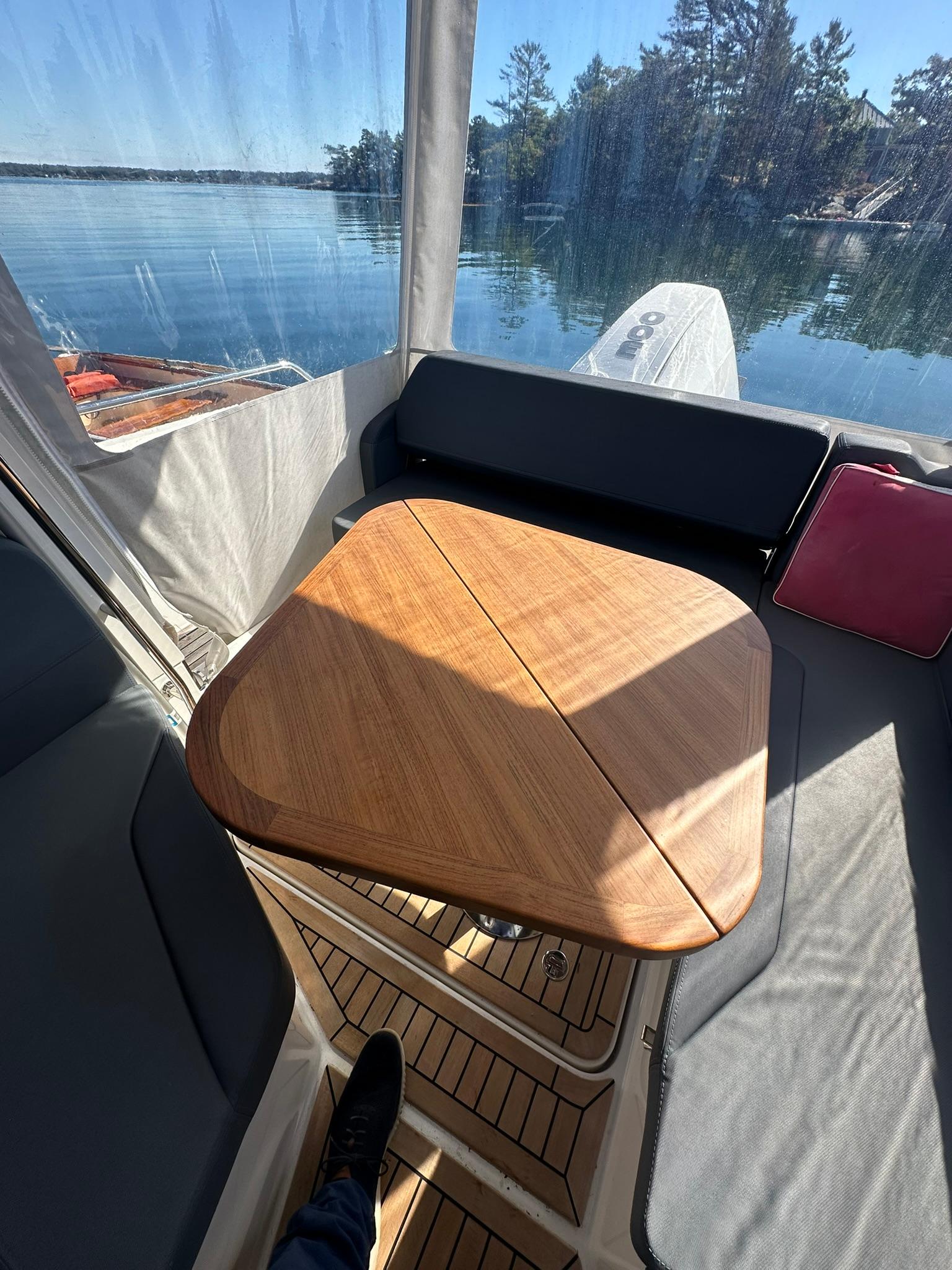 Cozy seating area on 2021 Nimbus W9 boat with wooden table and scenic lake view.
