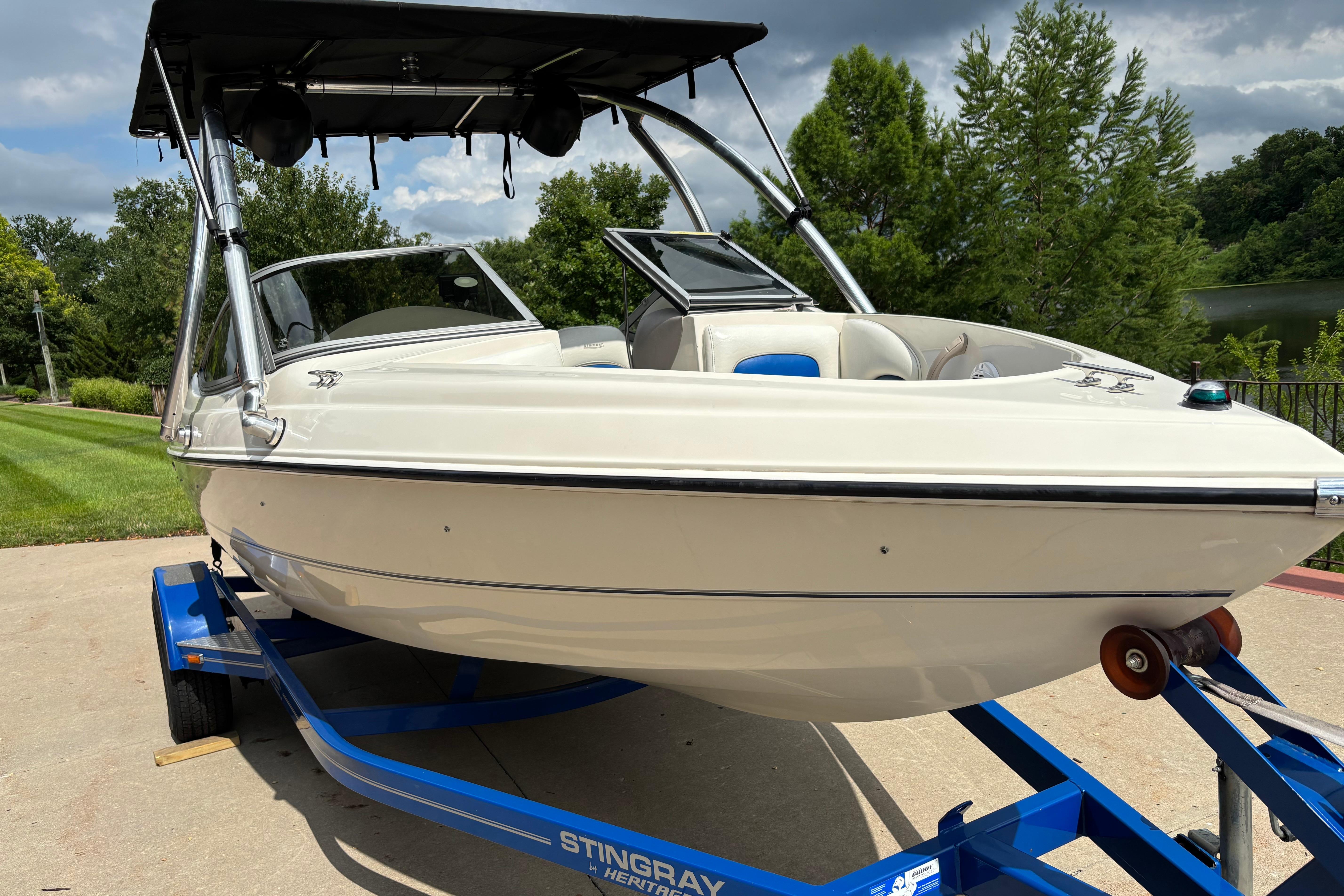 2007 Stingray 180 RX boat on trailer, parked outdoors with lush greenery background.
