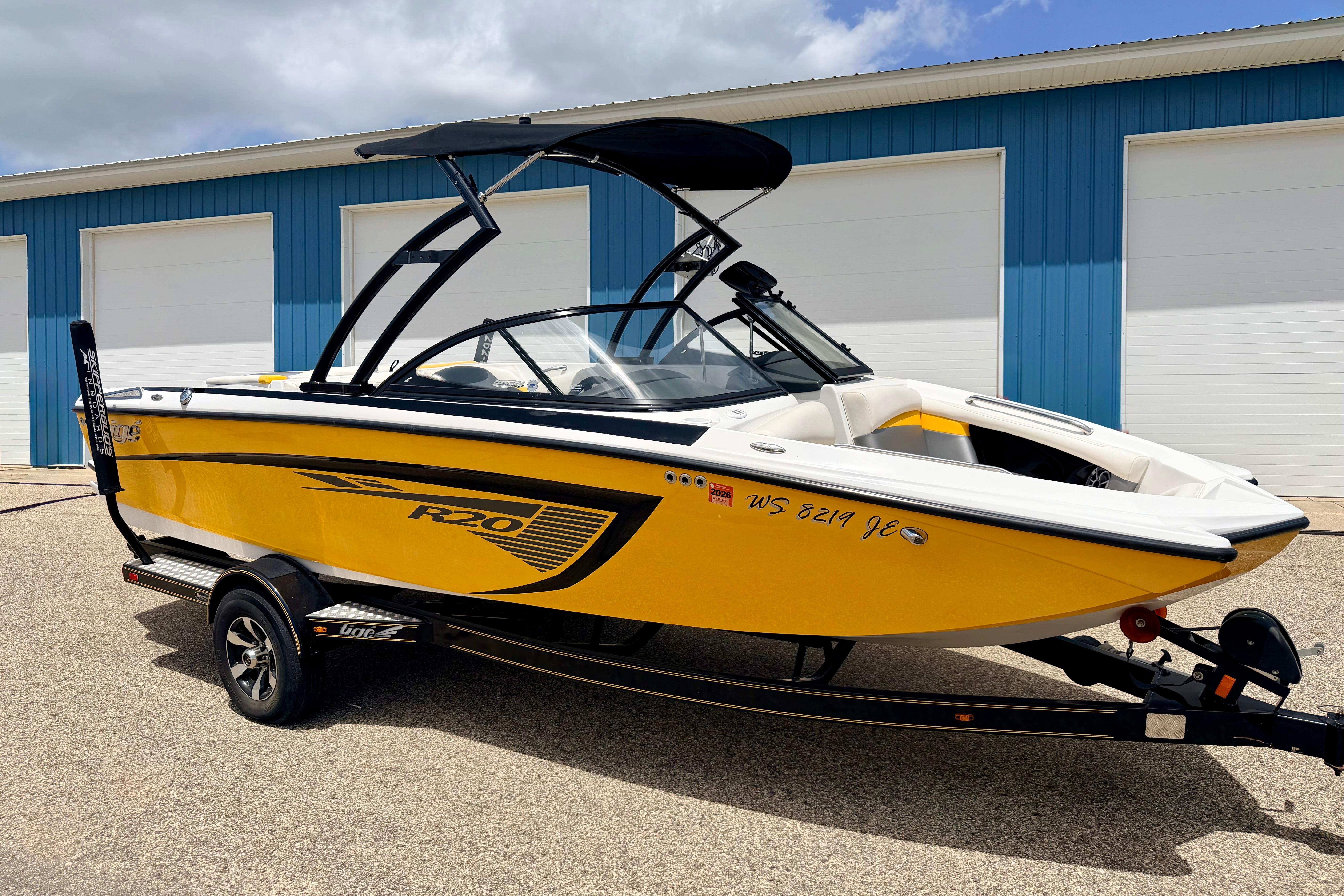 2014 Tigé R20 yellow boat on trailer, parked outside blue building.