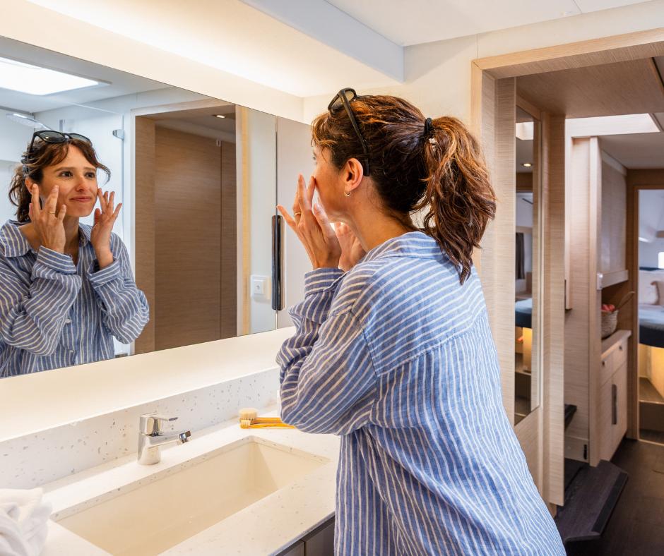 Woman in striped shirt applying skincare in Fountaine Pajot NEW 41 yacht bathroom, 2025 model.