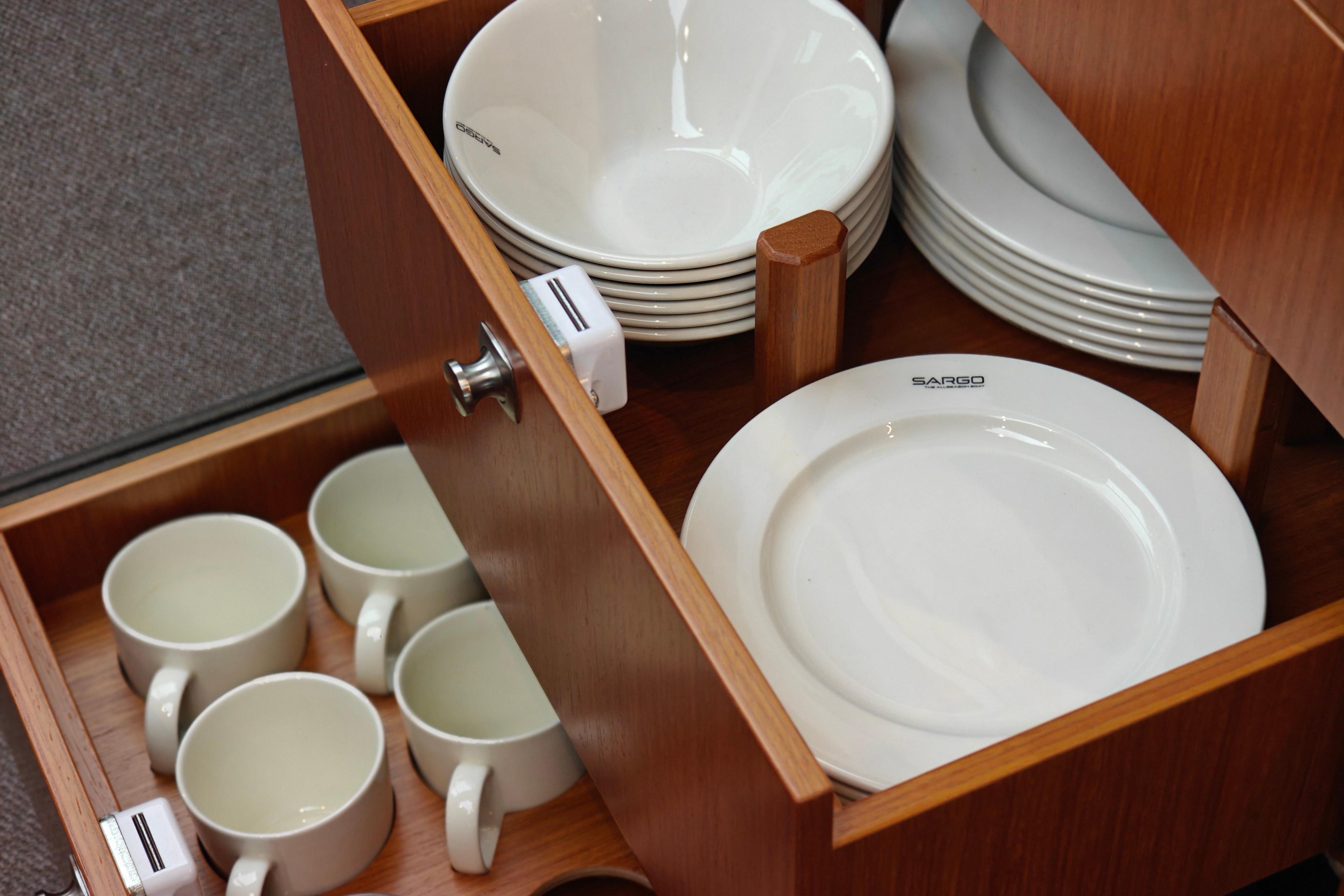 Open drawer with Sargo-branded plates and cups, showcasing elegant kitchenware storage.