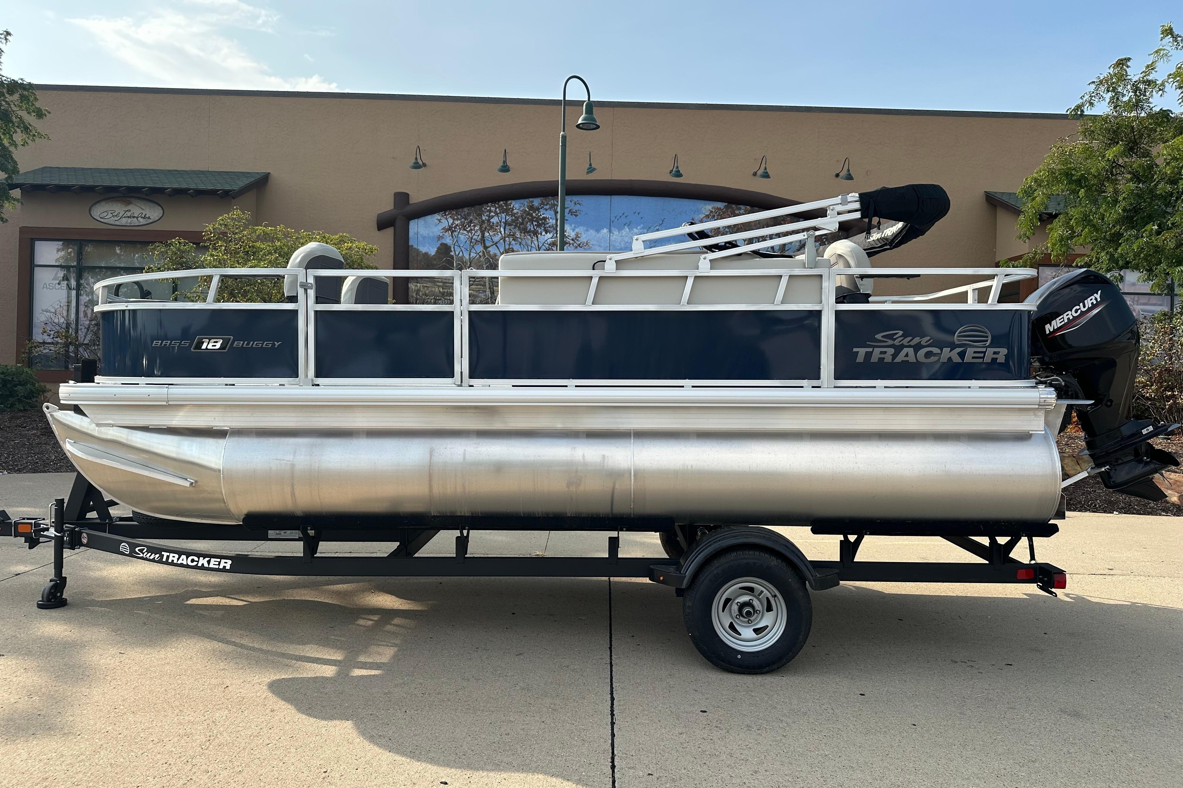 2026 Sun Tracker Bass Buggy 18 DLX pontoon boat on trailer, parked outdoors.
