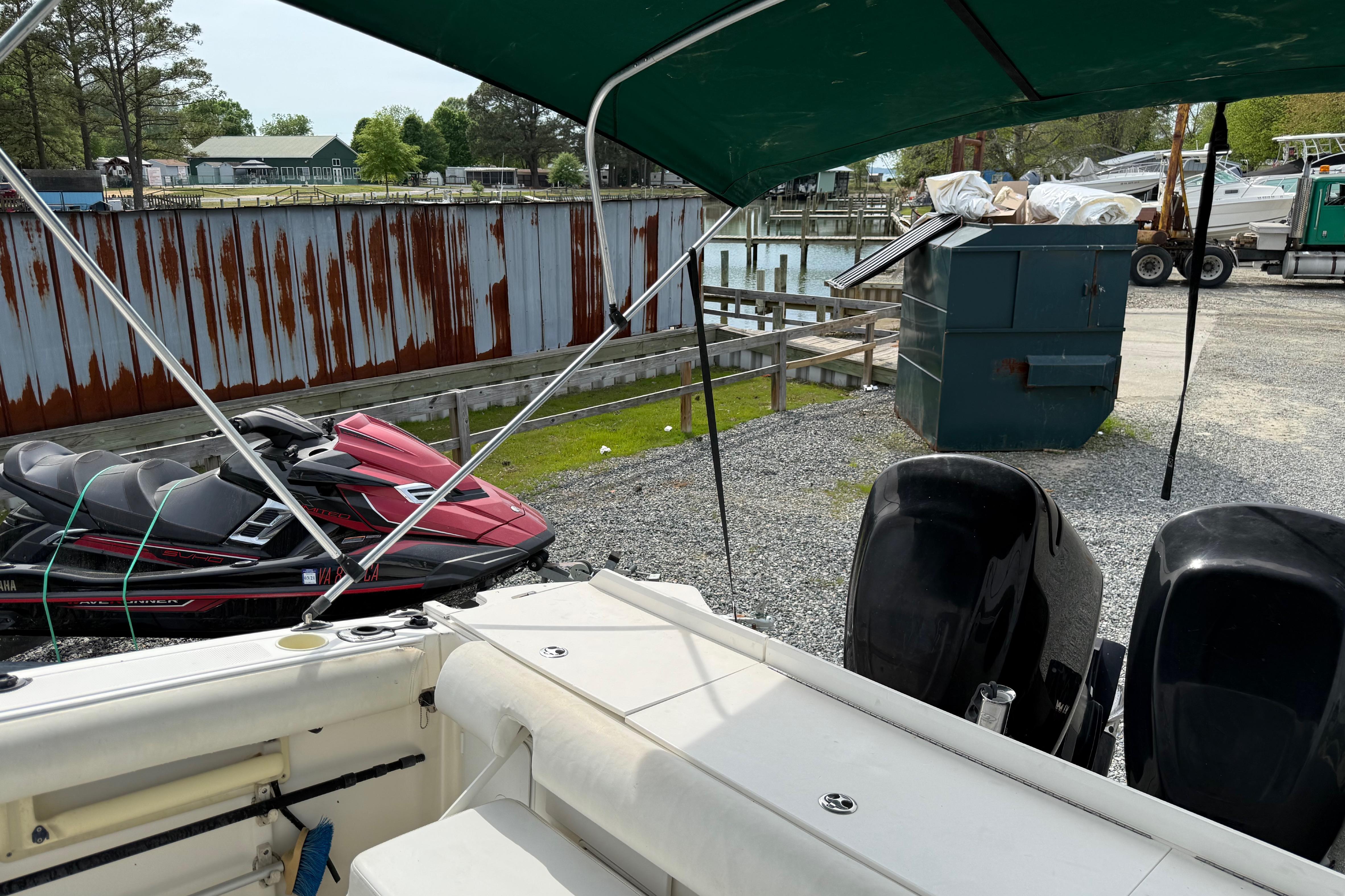 2006 Trophy 2502 Walkaround boat with dual engines, docked near jet skis and a rusted fence.
