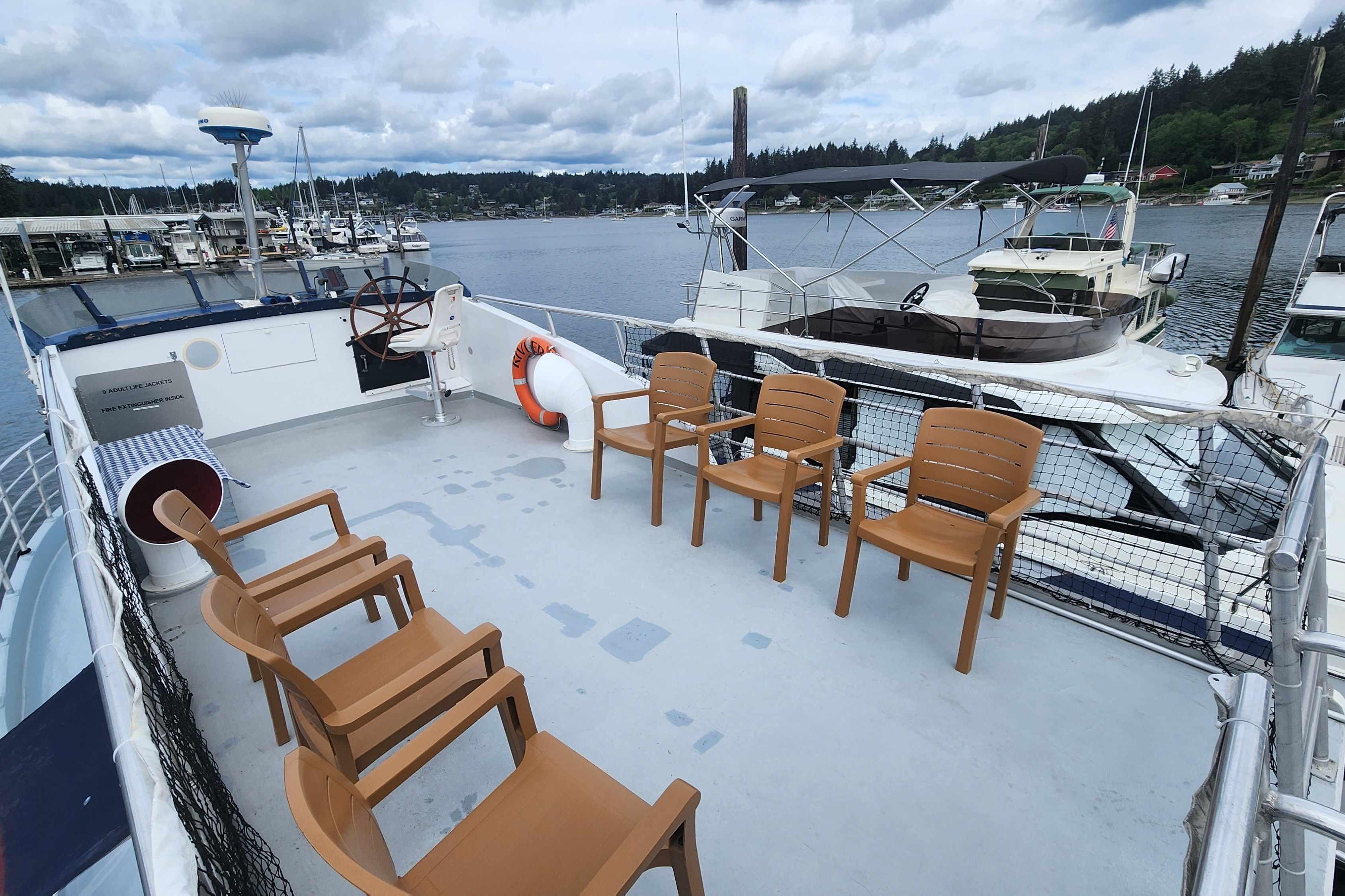 Upper deck of 1964 Grandy Tour Boat with chairs, overlooking marina and scenic water view.