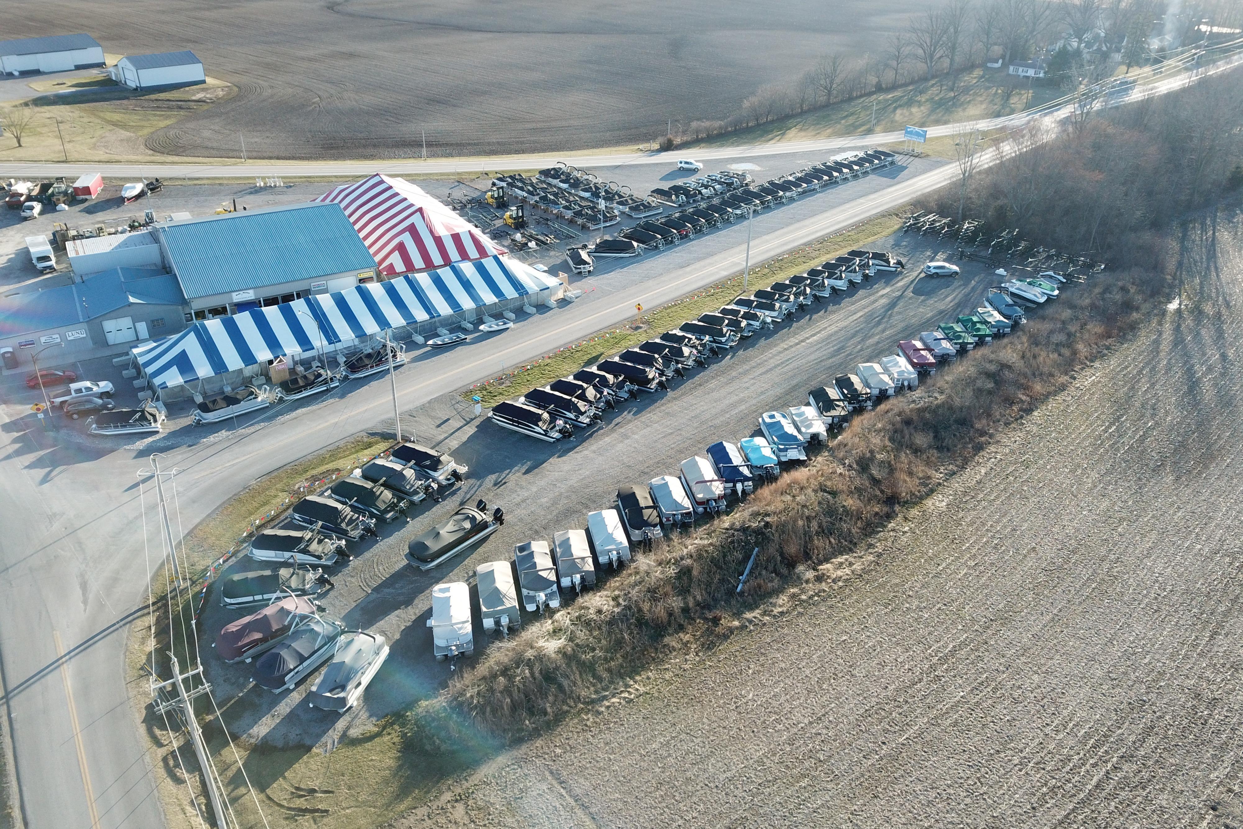 Aerial view of a boat dealership with striped tents and parked vehicles, featuring Barletta ARIA 22UC models.