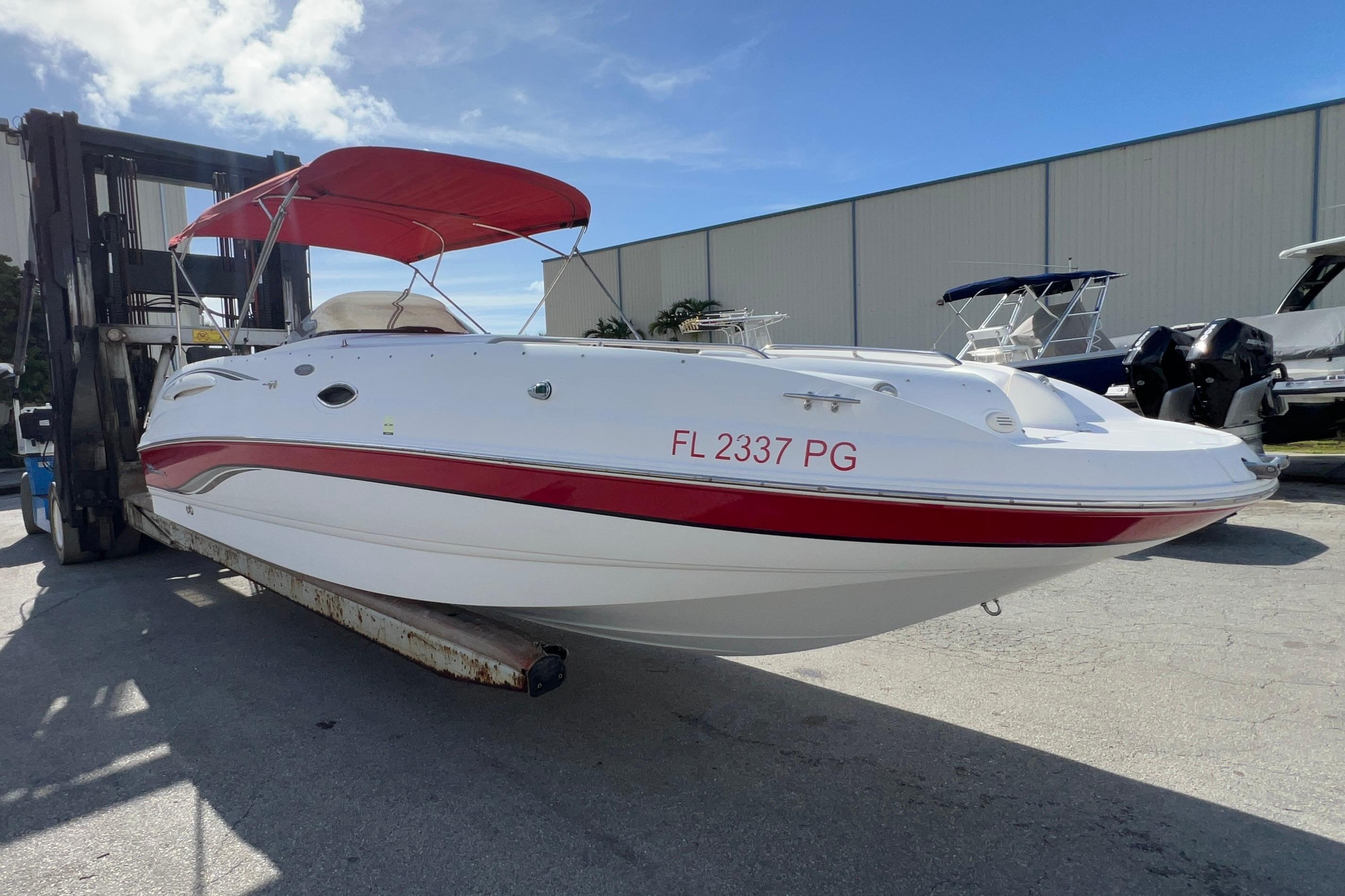 2002 Chaparral 232 Sunesta boat with red canopy on forklift, outdoor storage.