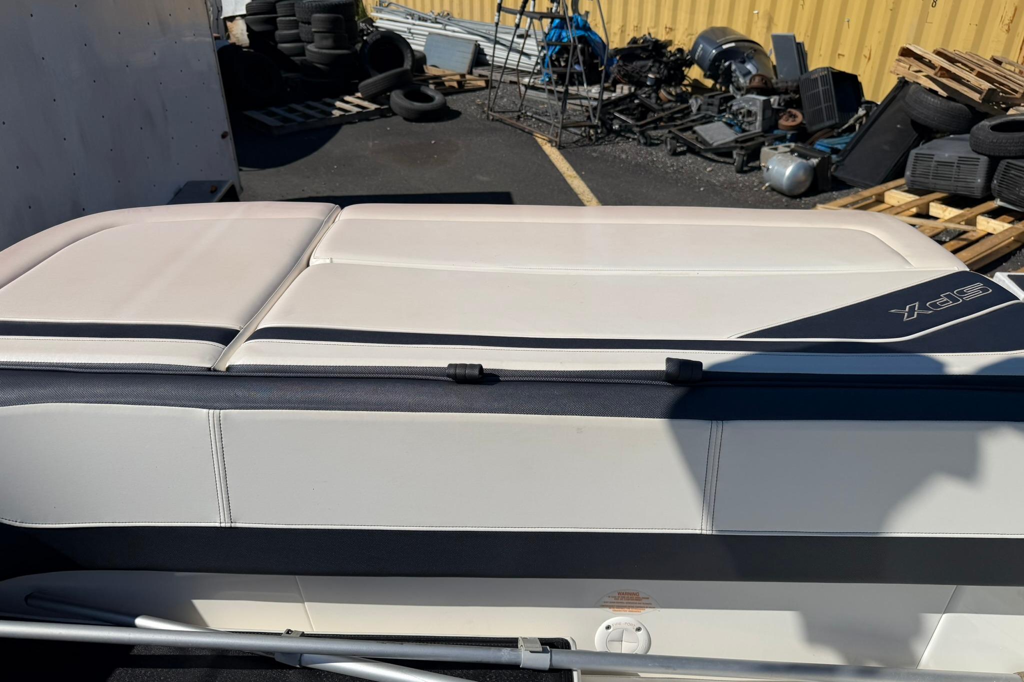 2016 Sea Ray SPX 210 boat interior with white seating, parked near tires and equipment.