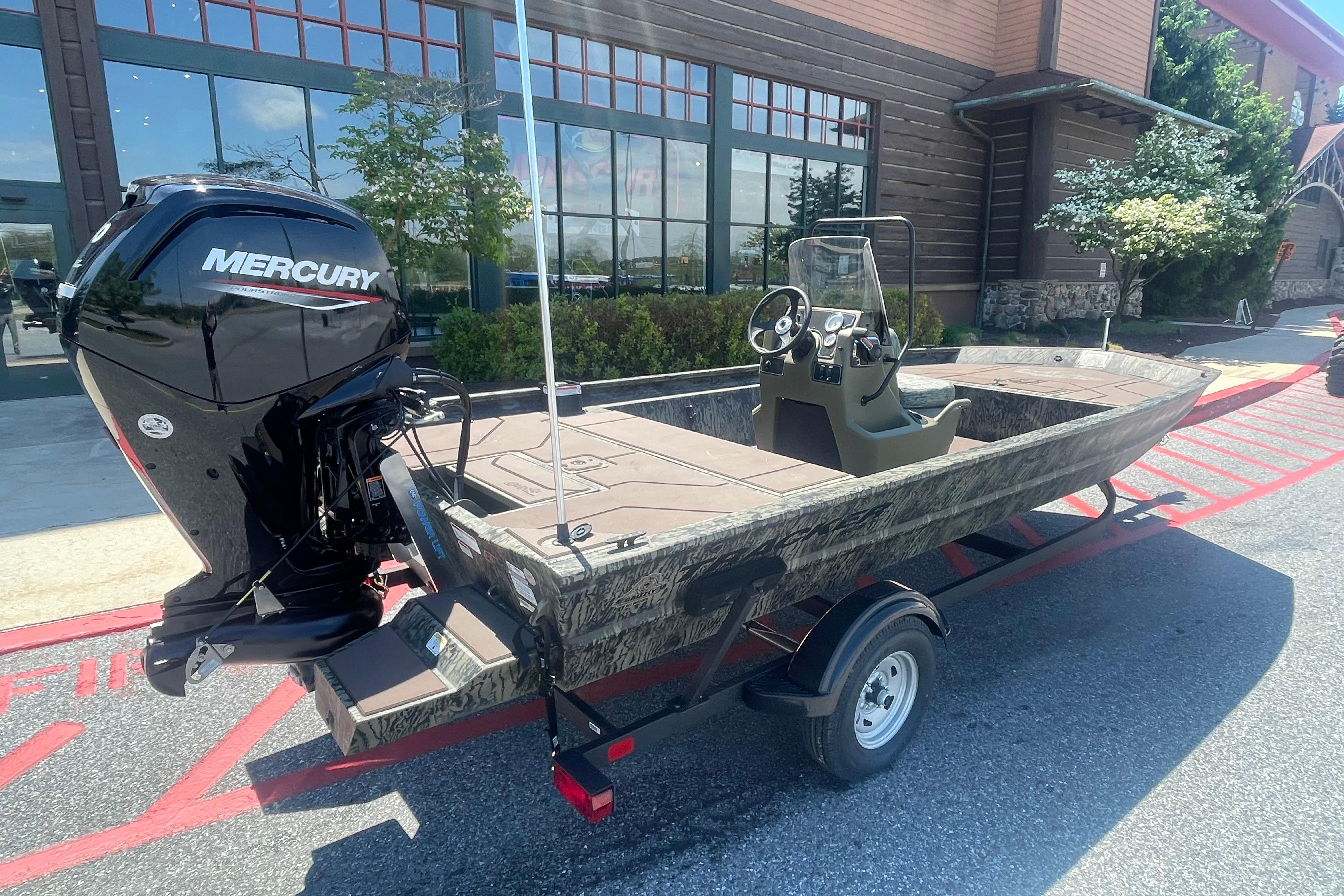 2026 Tracker Grizzly 1860 CC boat with Mercury engine, parked outside a building.