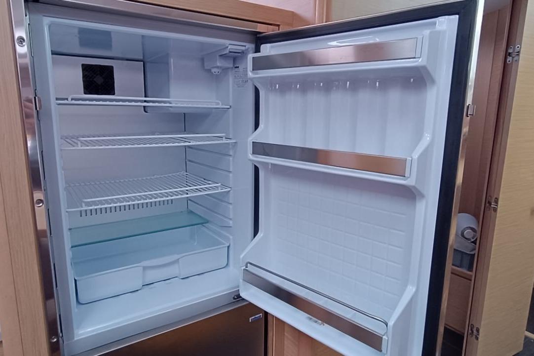 Open refrigerator inside a 2024 Dufour 470 yacht, showcasing spacious interior shelves.