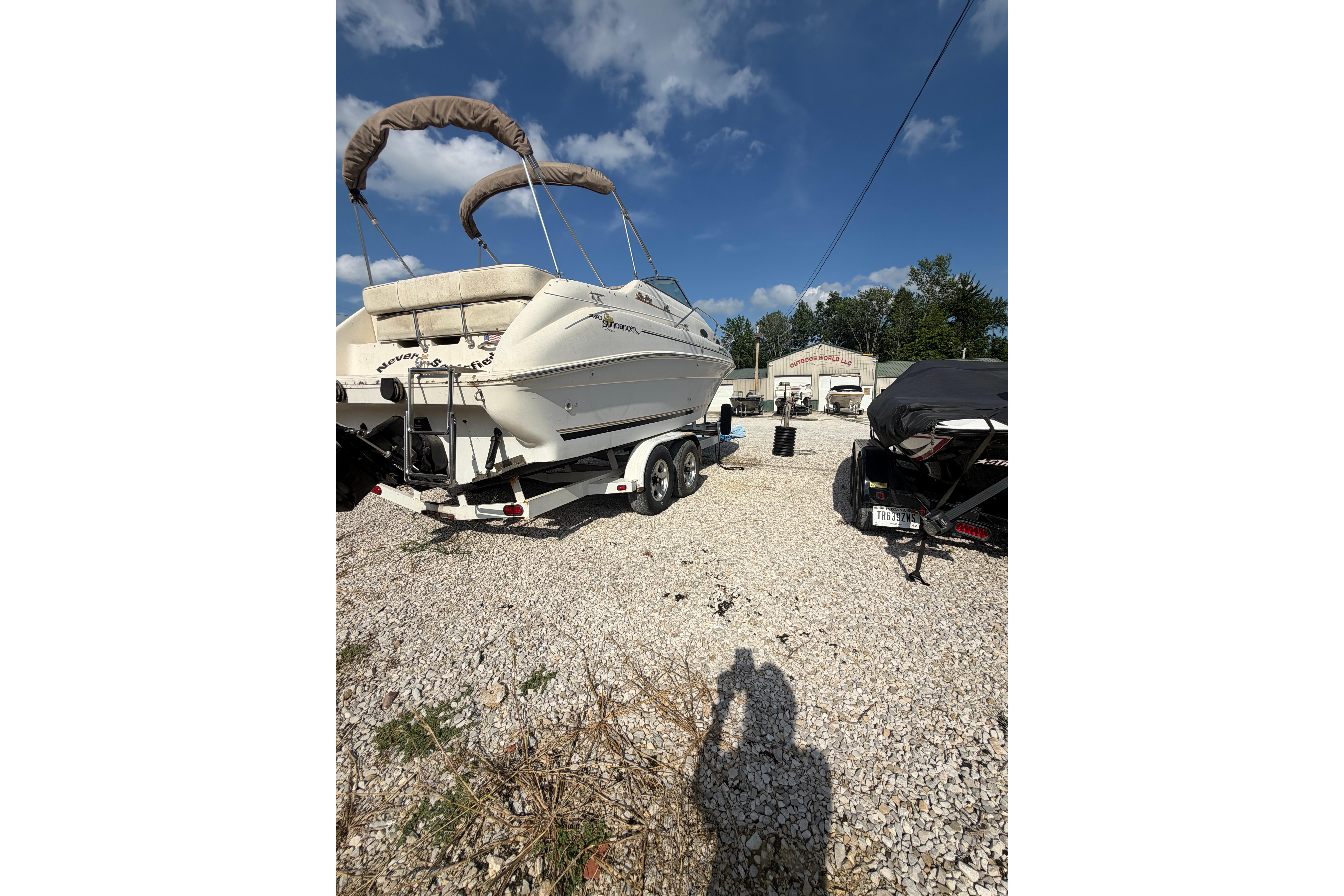 1999 Sea Ray 240 Sundancer boat on trailer, parked outdoors under a clear blue sky.
