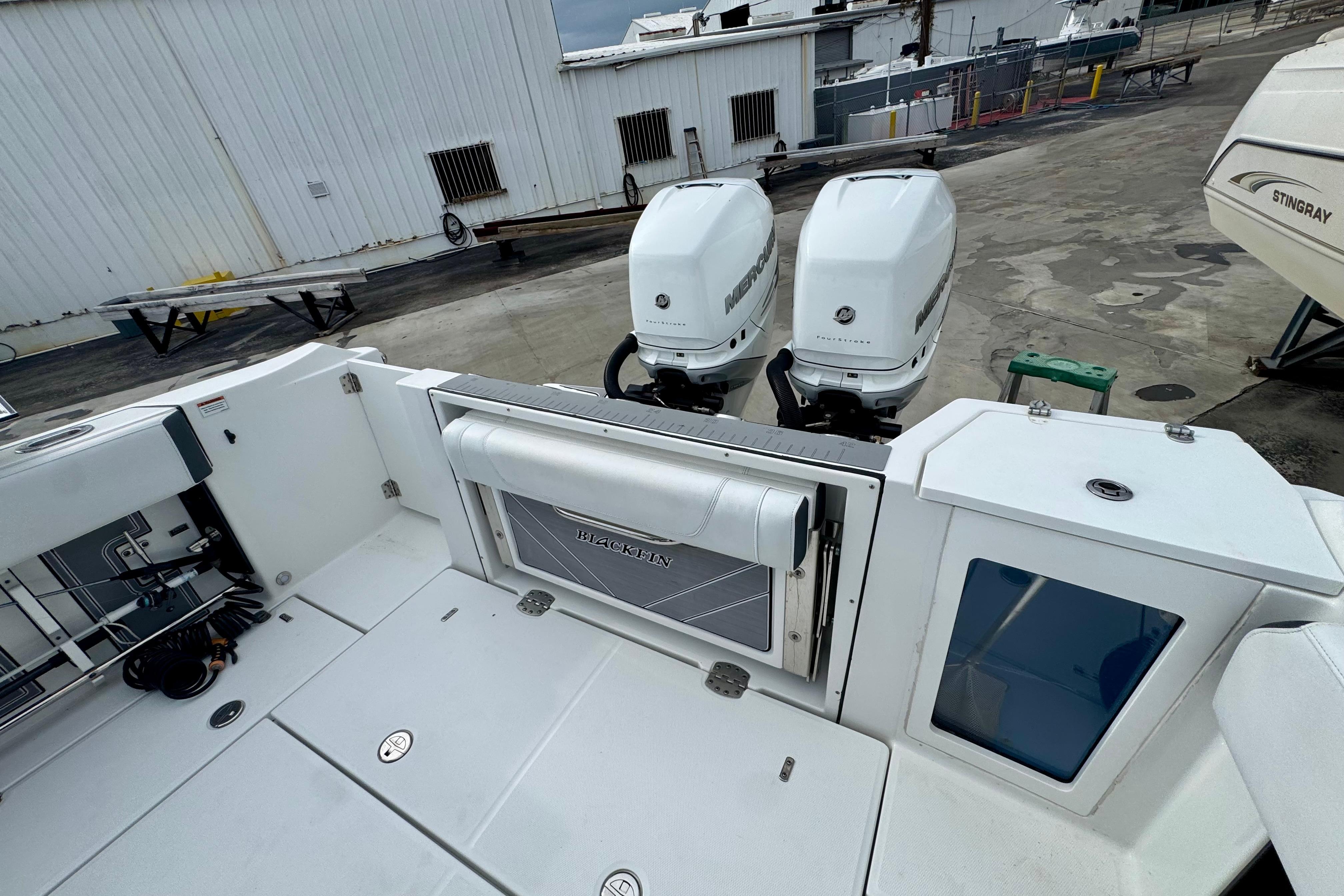 2023 Blackfin 332 CC boat with dual Mercury outboard engines, docked near a warehouse.