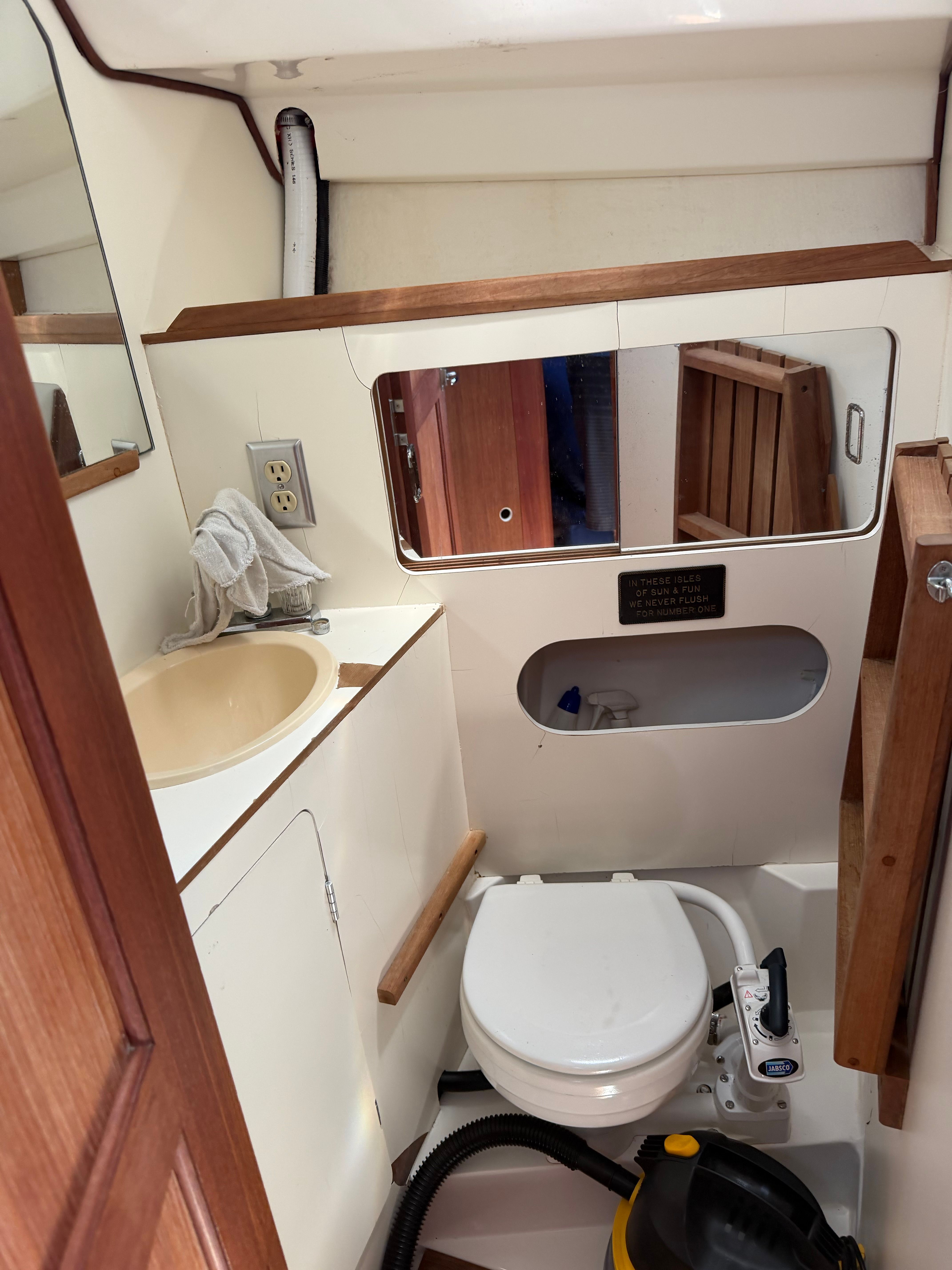 The image shows a boat bathroom with a toilet, sink, and mirror.