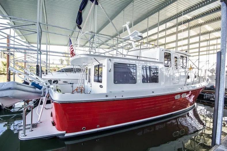 2006 American Tug AT boat with red hull docked under a covered marina.