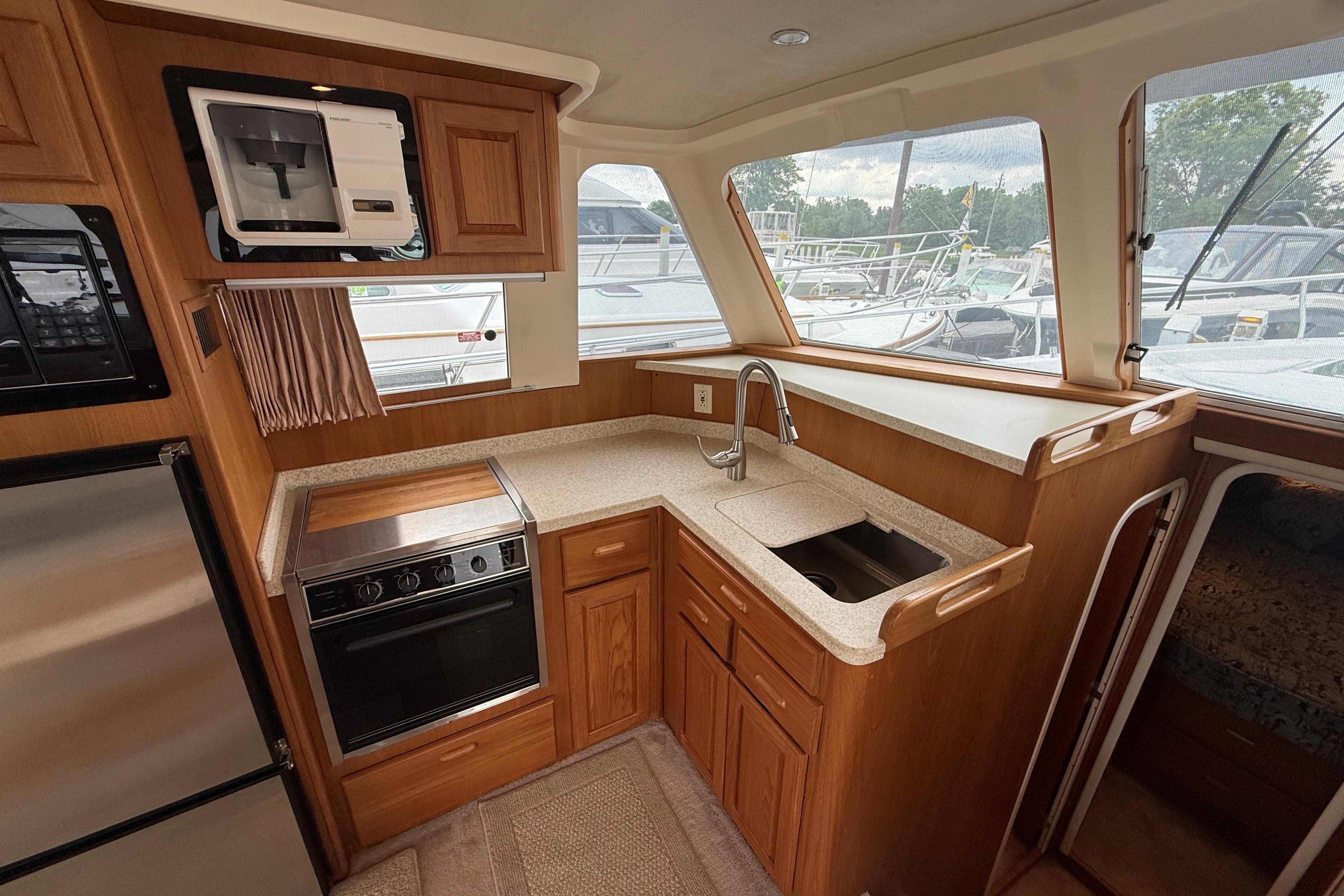 1999 Mainship 350 Trawler kitchen with wood cabinetry, stainless steel appliances, and large windows.