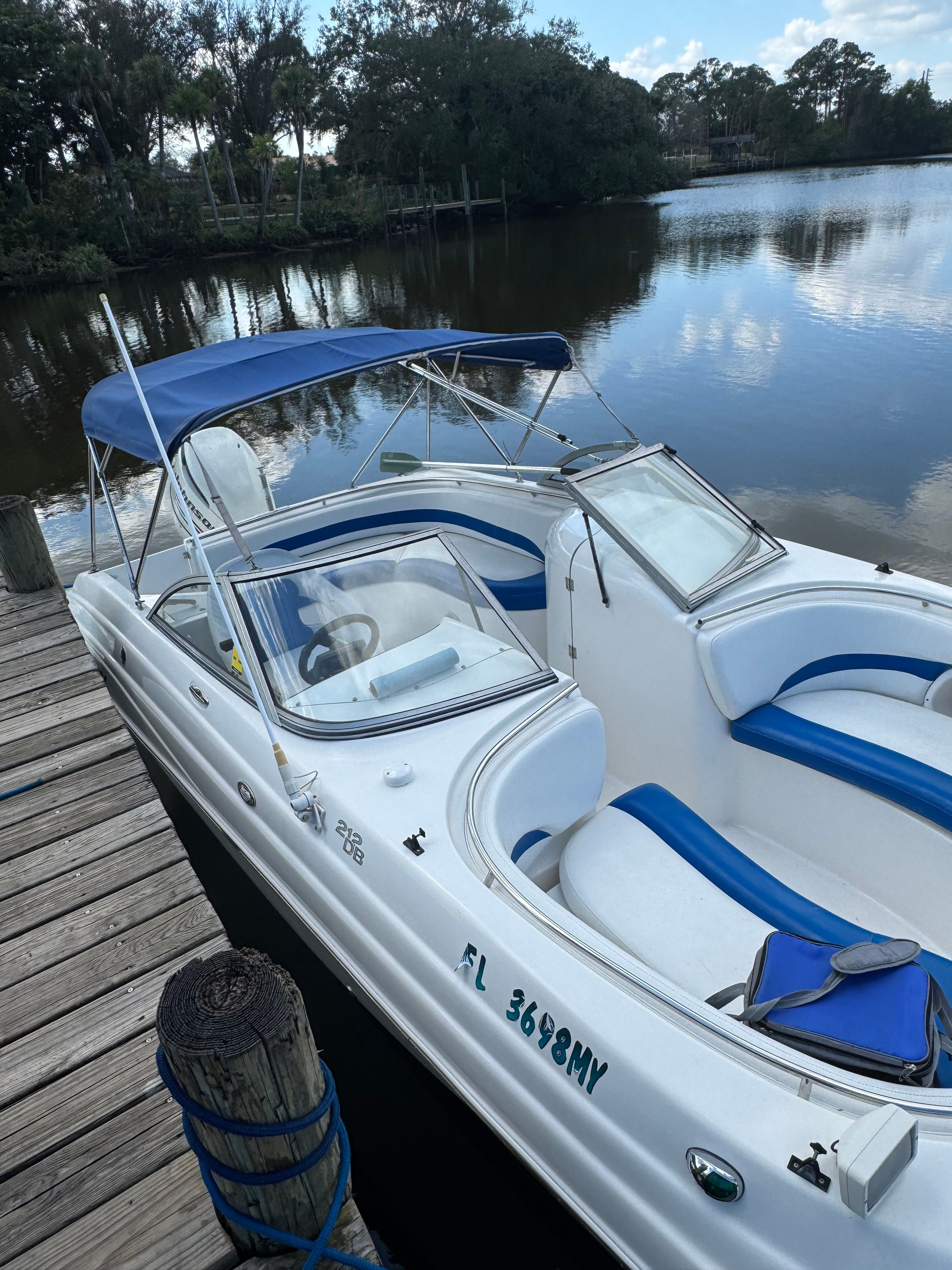 A white boat with blue seats and a blue sunshade docked at a wooden pier.