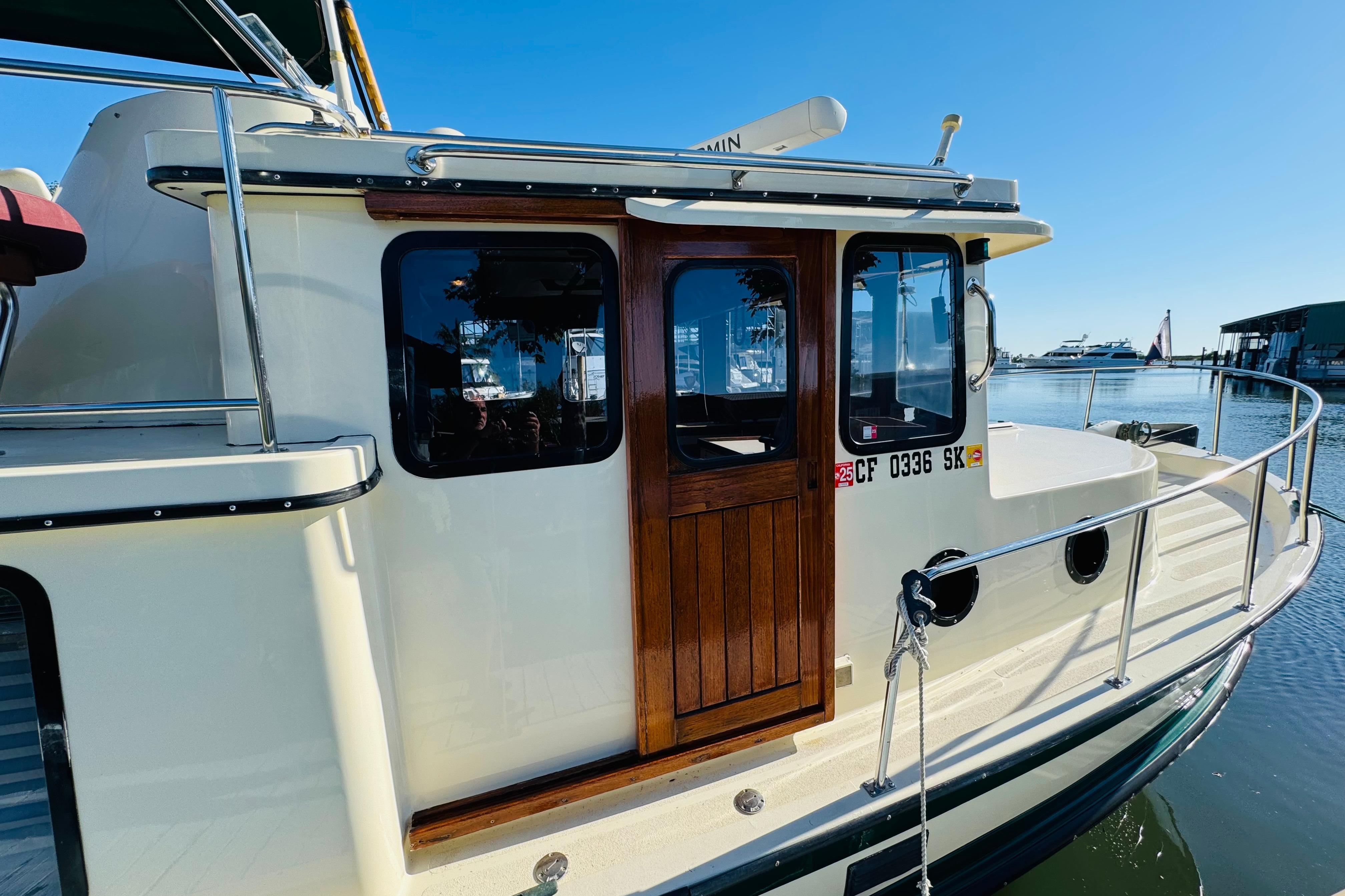 1996 Nordic Tug 32 docked, showcasing wooden door and windows, with clear blue sky background.