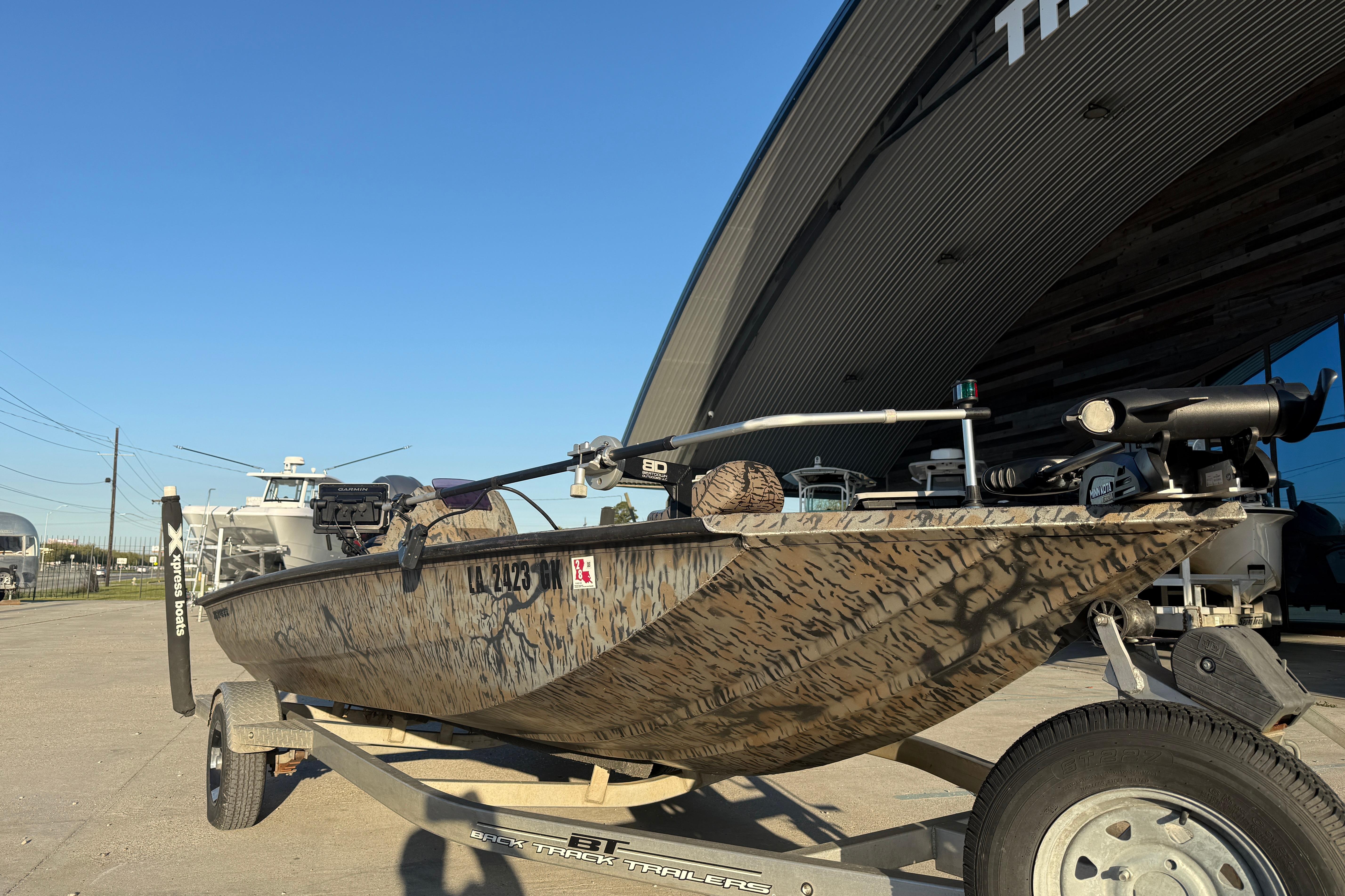 2019 Xpress XP7 boat with camouflage design on a trailer, parked outside a building.