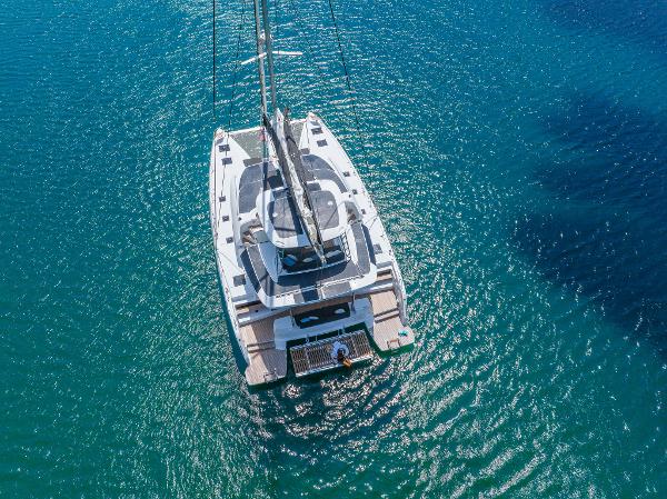 Aerial view of 2025 Lagoon 51 ICONIC catamaran sailing on clear blue water.
