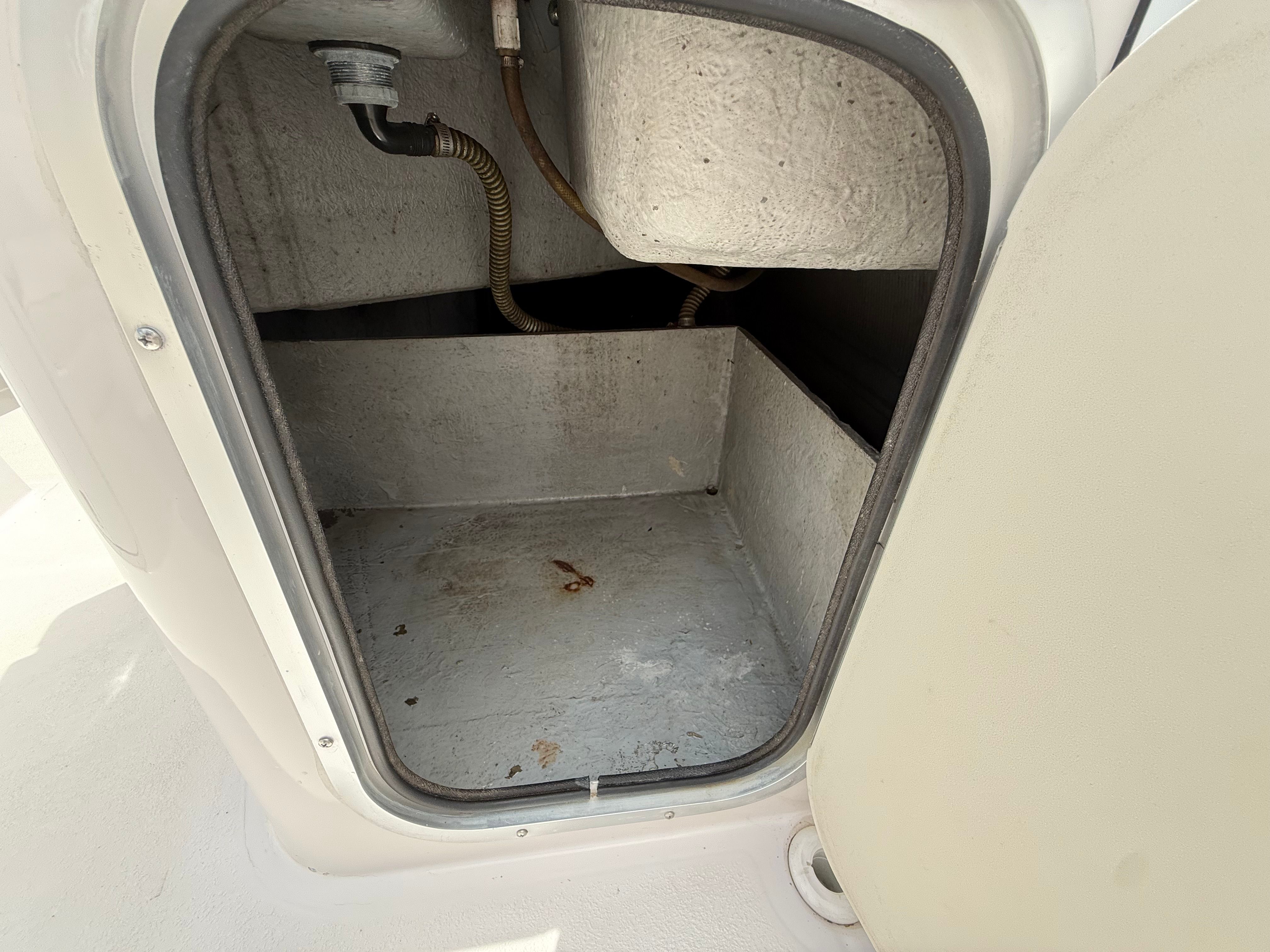 An open storage compartment on a boat with a drain pipe and gray interior surface.