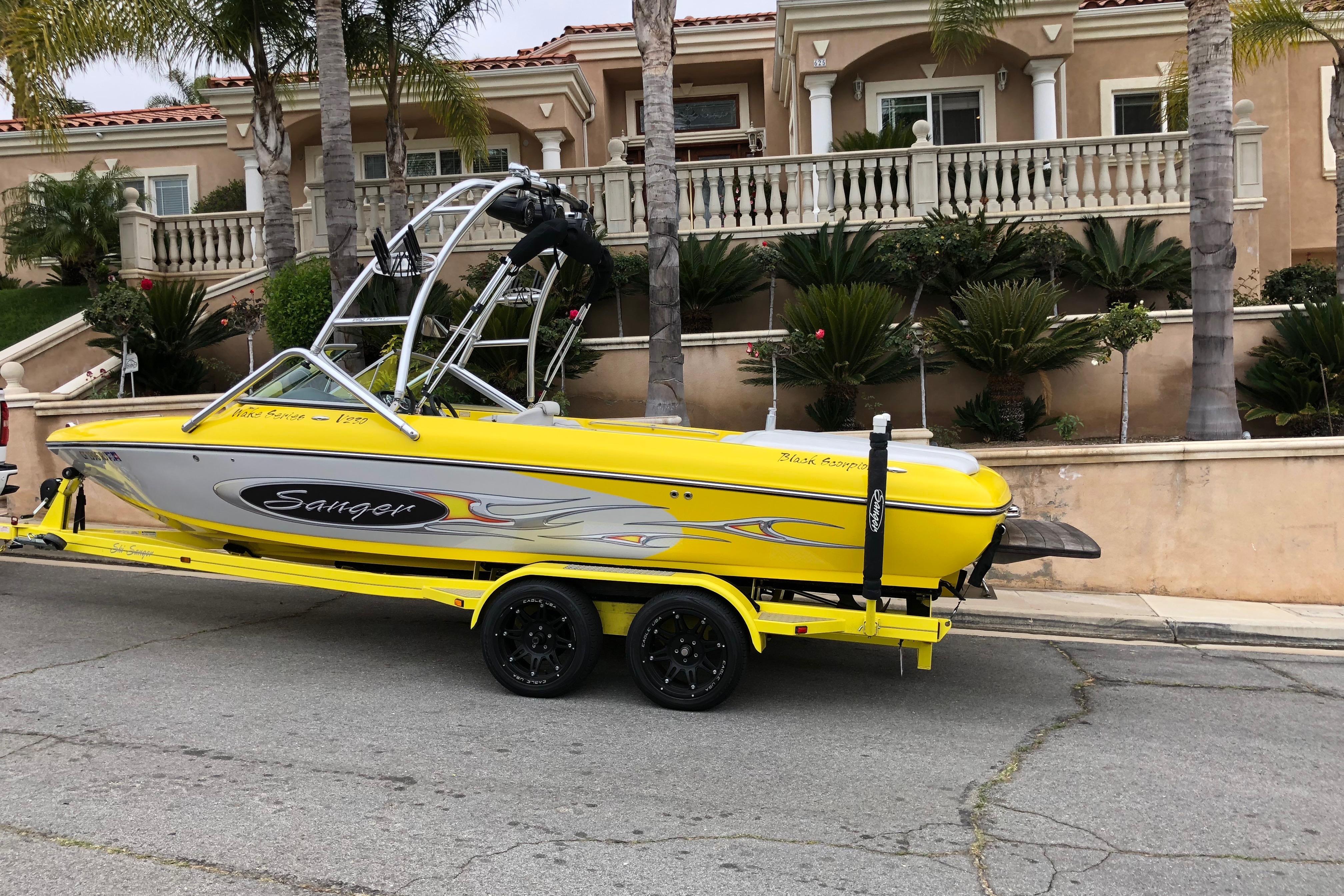 Yellow 2006 Sanger V230 boat on trailer, parked in front of a luxurious house.