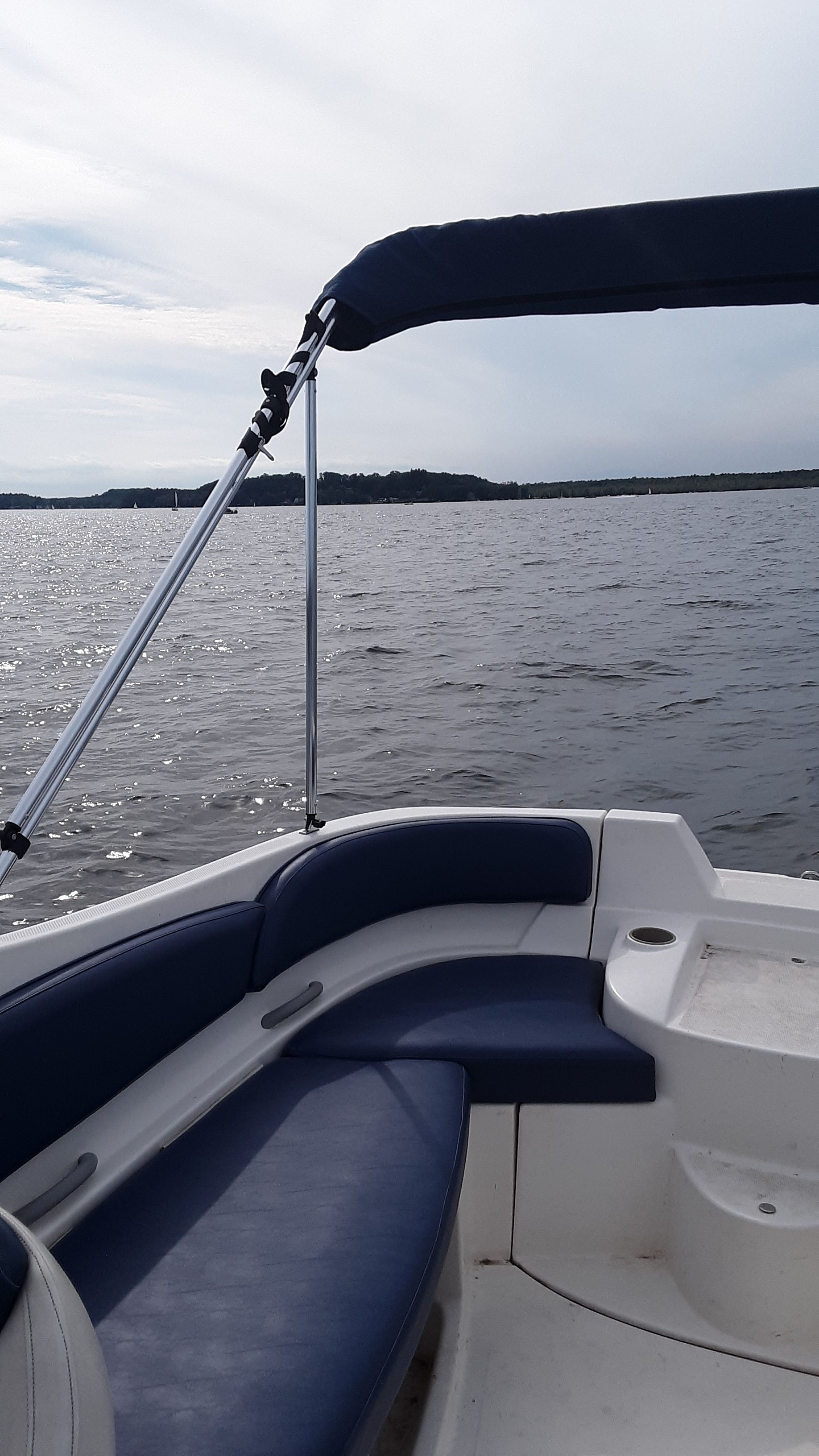 2005 Bayliner 210 Classic with blue seating and a Bimini top on calm water.