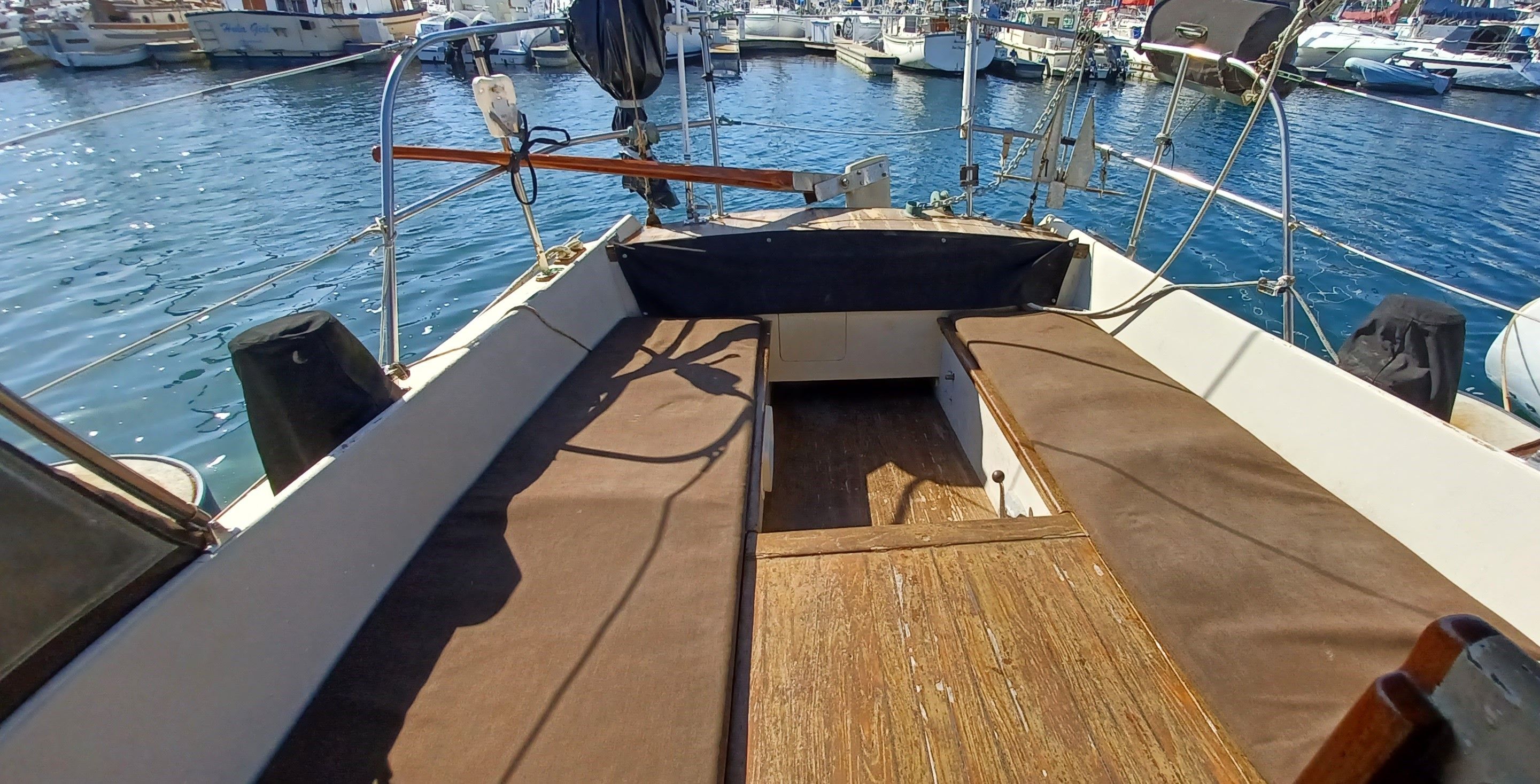 The deck of a sailboat in a marina with brown cushions and wooden details.
