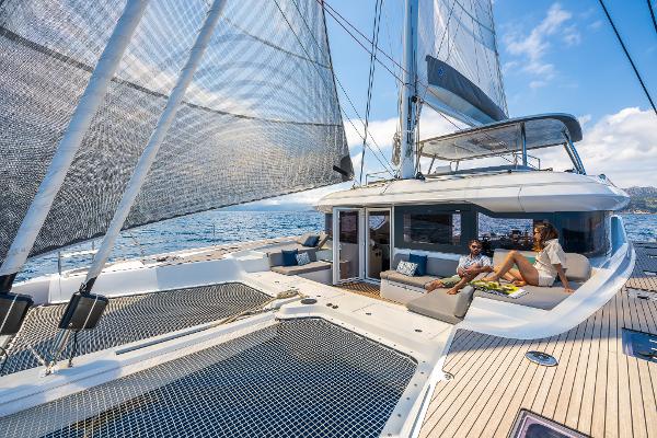 2025 Lagoon 60 catamaran sailing with people relaxing on deck, under clear blue skies.