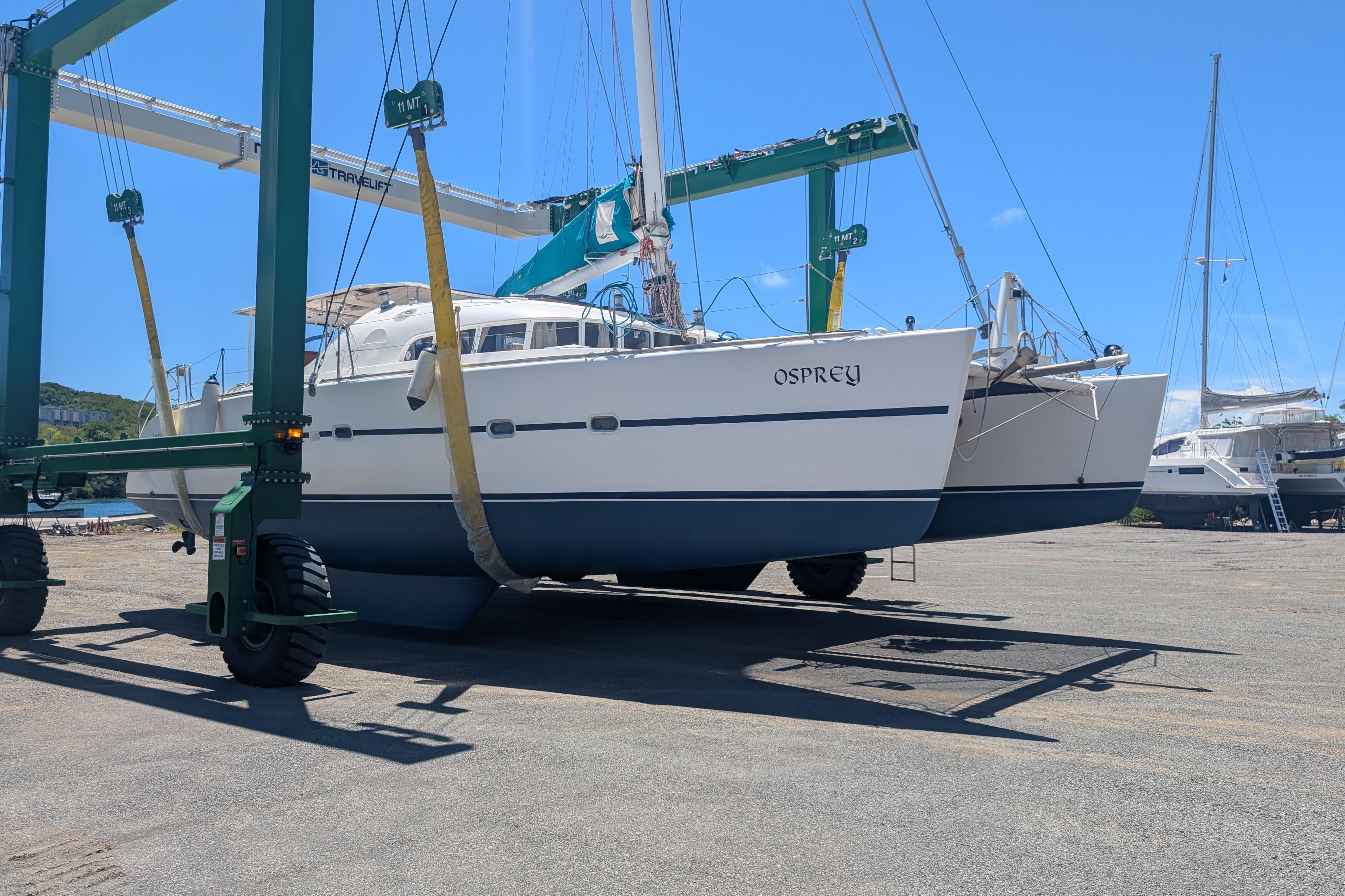Catamaran "Osprey" Lagoon 470, 2002 model, on a boat lift in a sunny marina.
