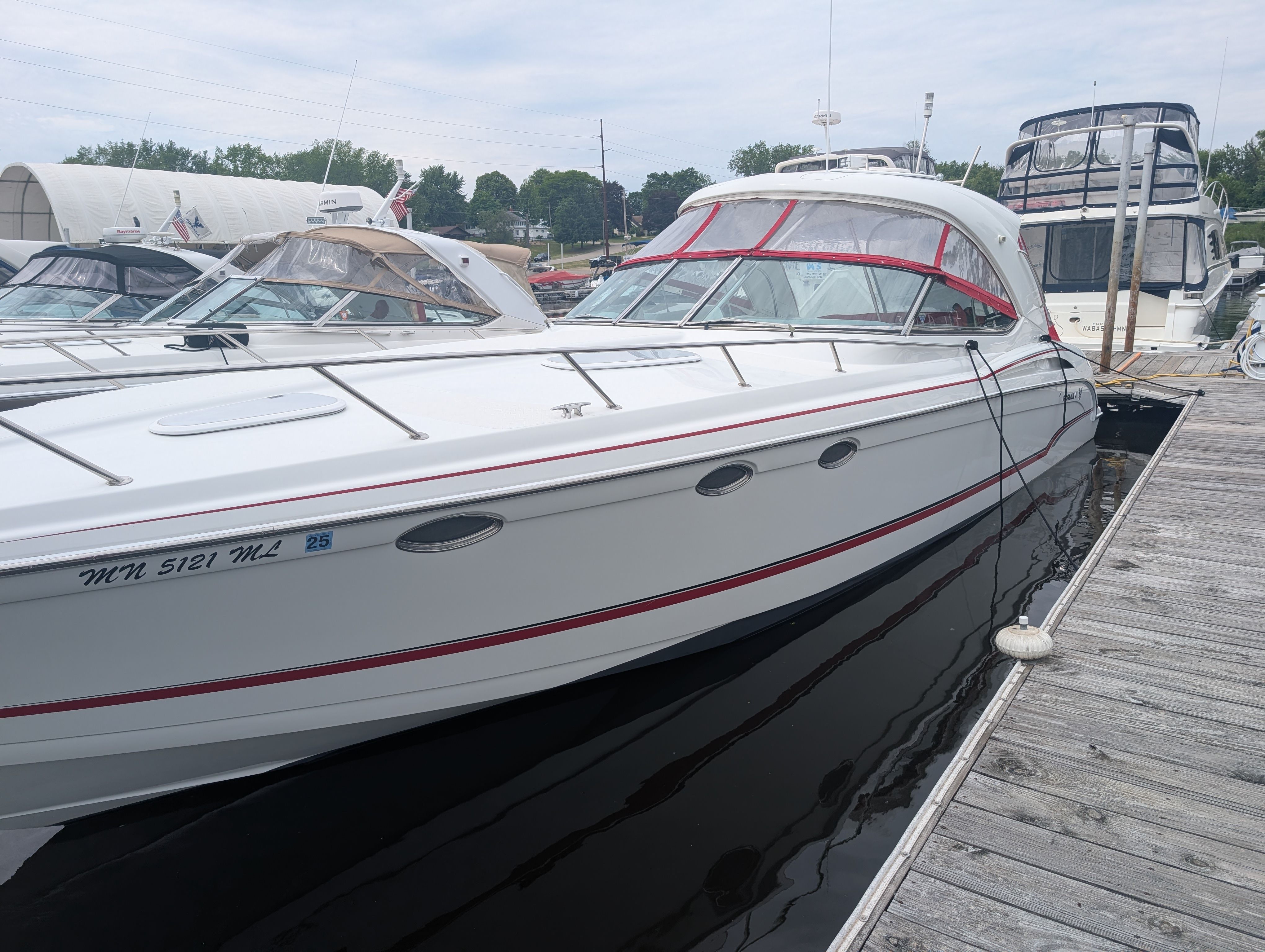 A white motor yacht docked at a wooden pier. It features red accents and an enclosed cockpit.