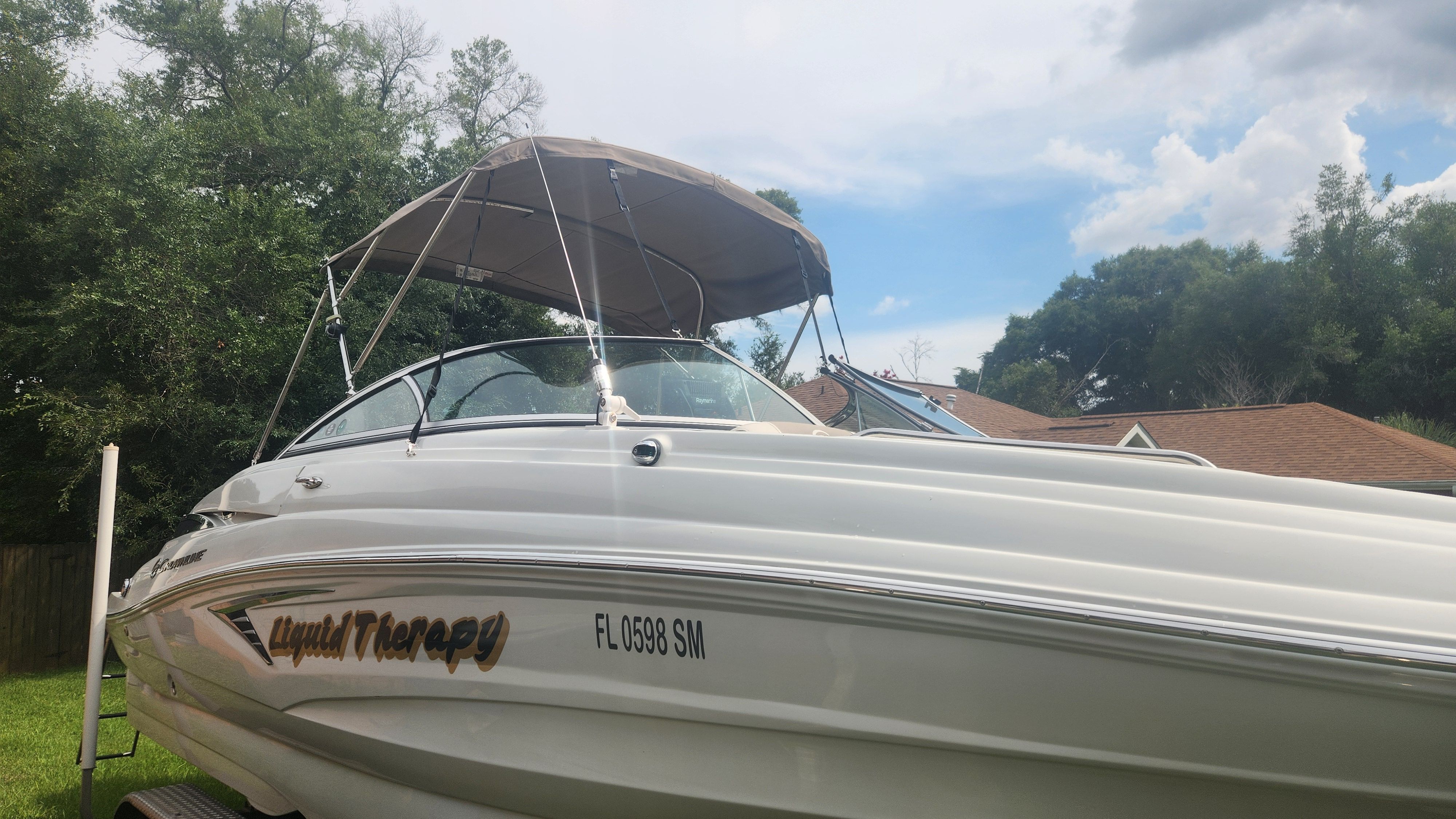 A white 2019 Crownline Eclipse E235 XS boat with a bimini top, parked on a lawn.