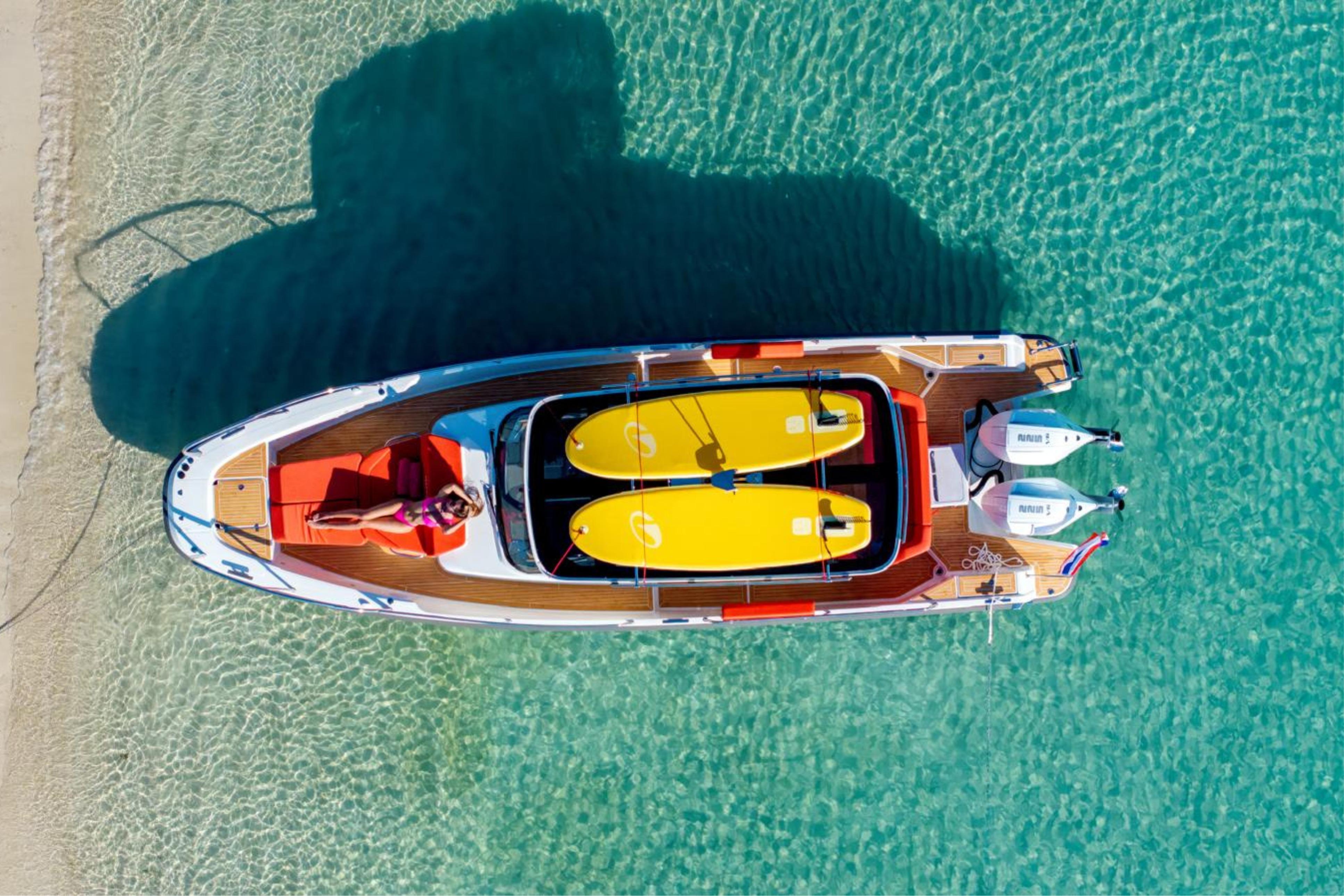 2024 Nimbus Tender 9 boat anchored in clear turquoise water, featuring paddleboards and sunbathing area.