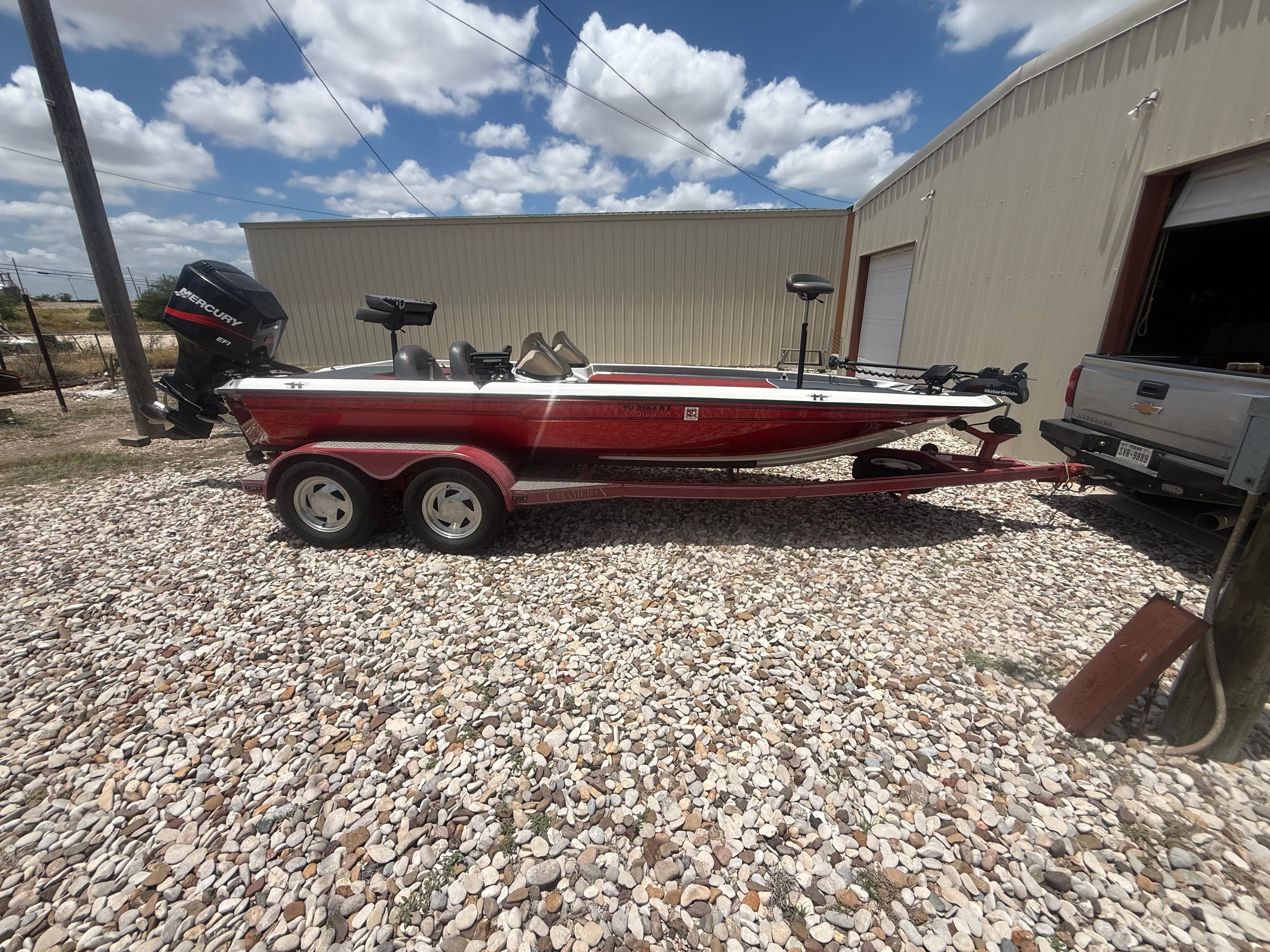 A red 1999 Champion 202 boat on a trailer beside a building.