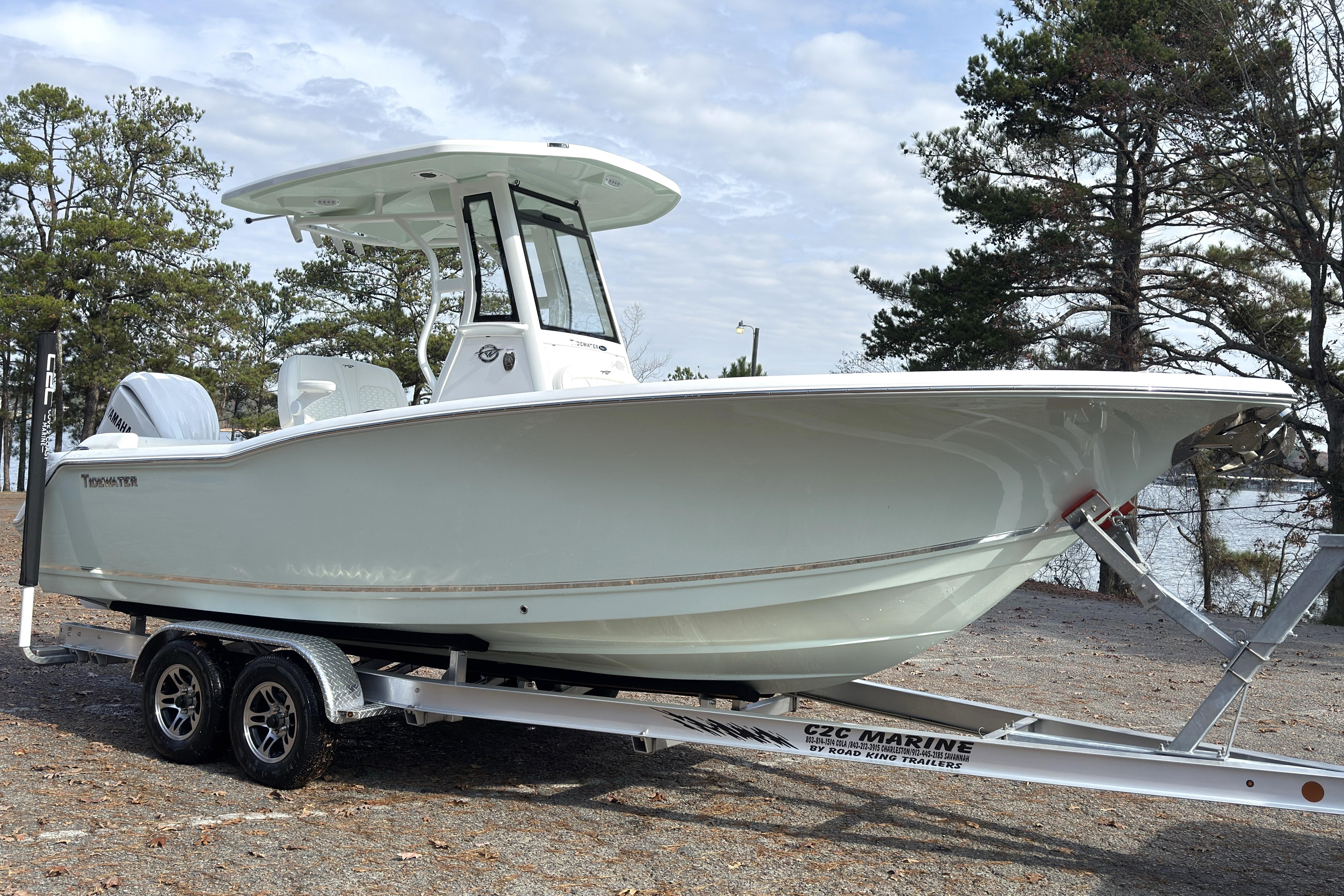 2026 Tidewater 232 LXF boat on trailer, parked outdoors near trees and water.