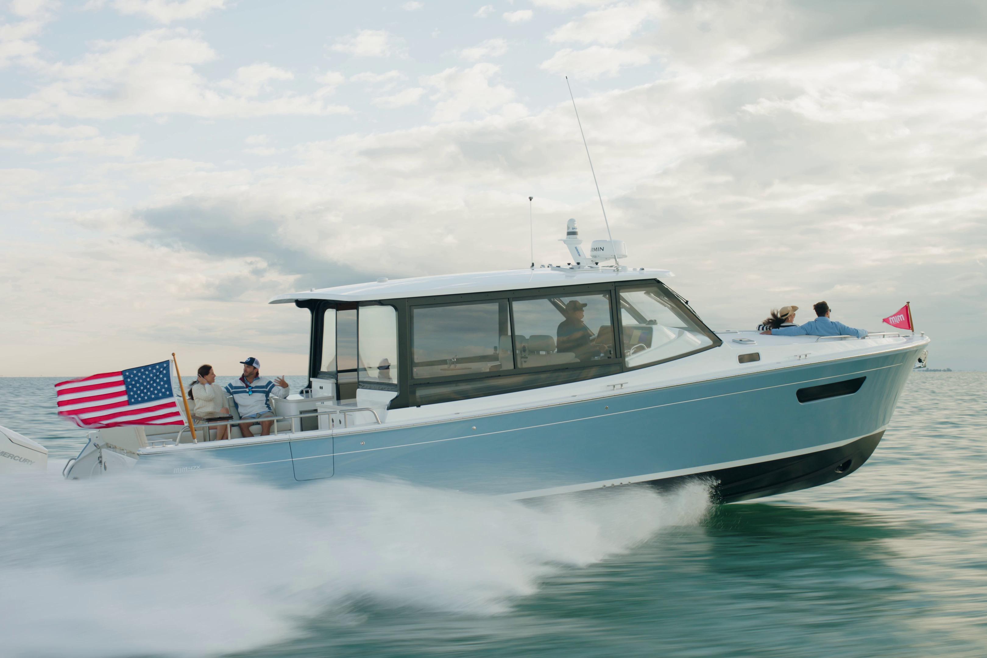 2026 MJM 47X boat cruising on open water with passengers, American flag waving.