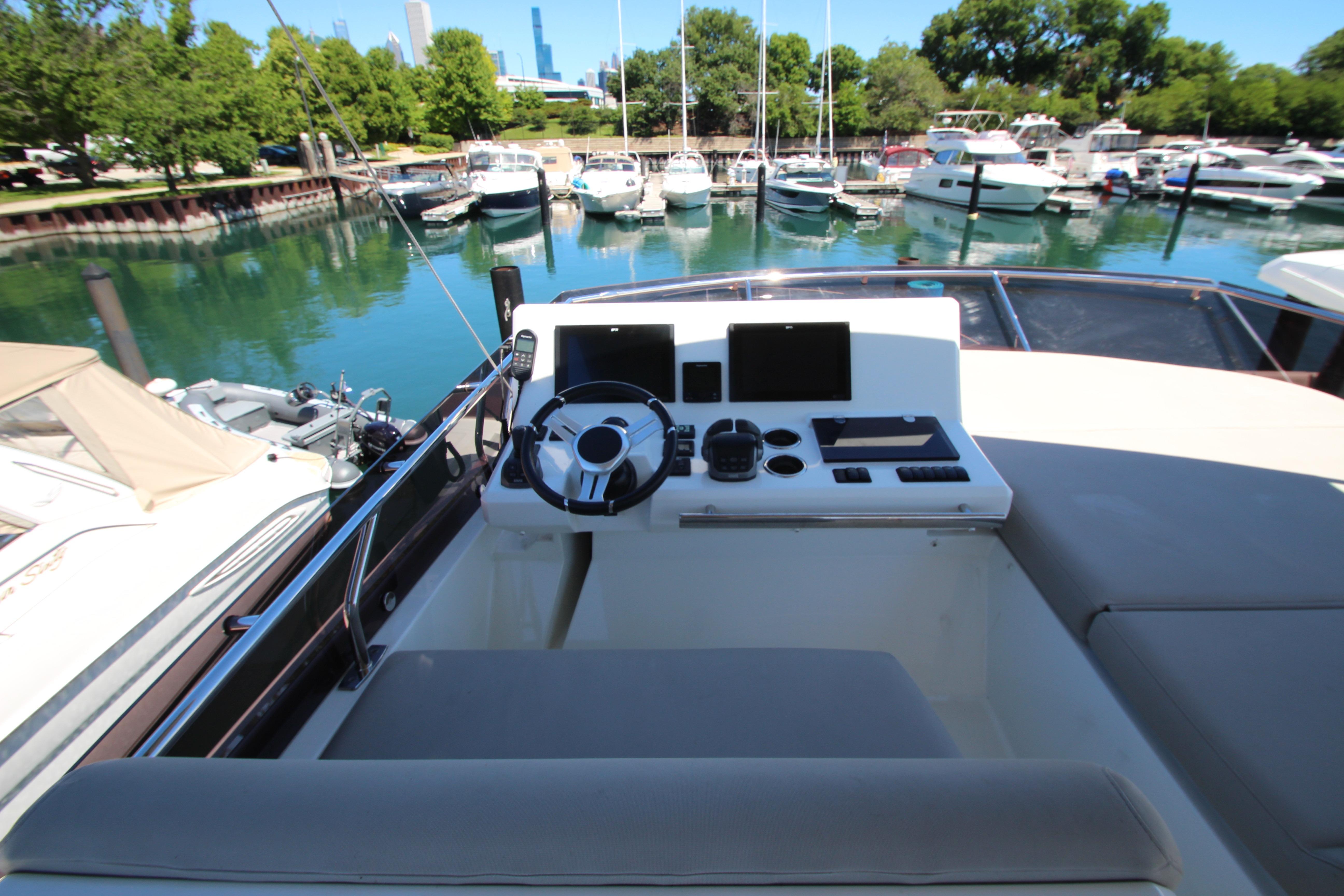 Cockpit of 2022 Prestige 520 yacht docked in a marina with lush greenery.
