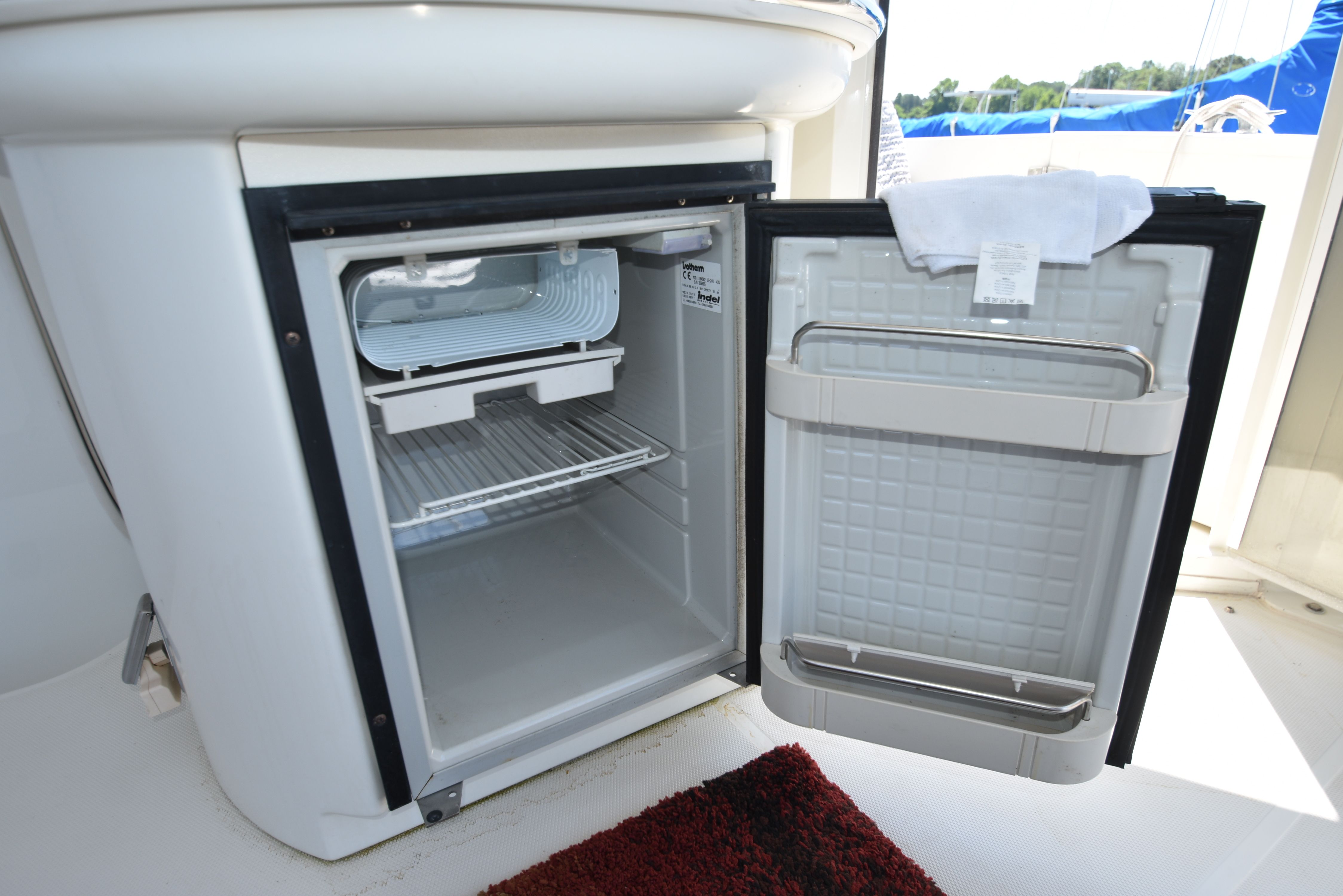 An open refrigerator on a yacht with a towel on the door.