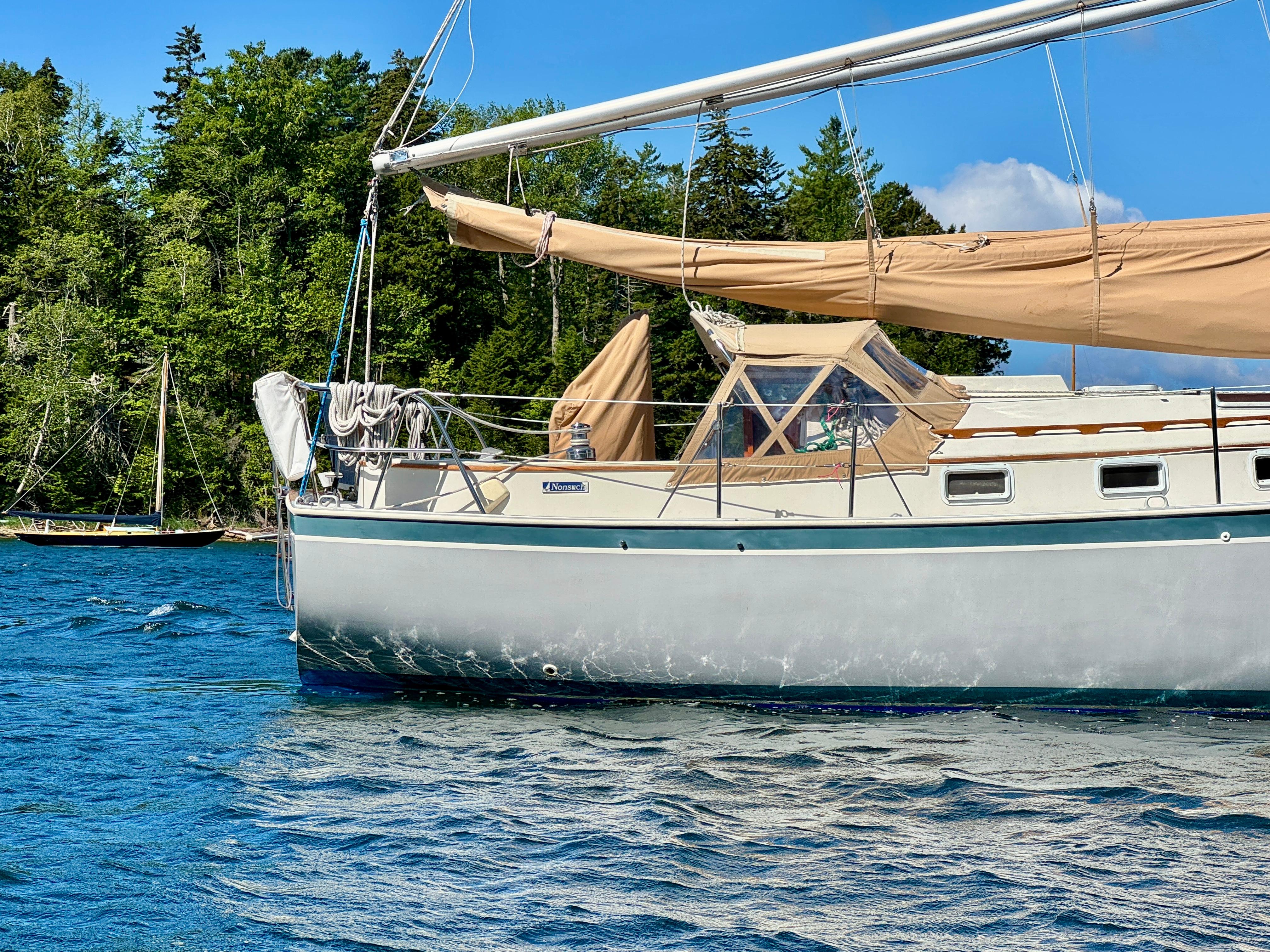 1989 Nonsuch 30 Ultra sailboat on a serene lake with lush green trees.