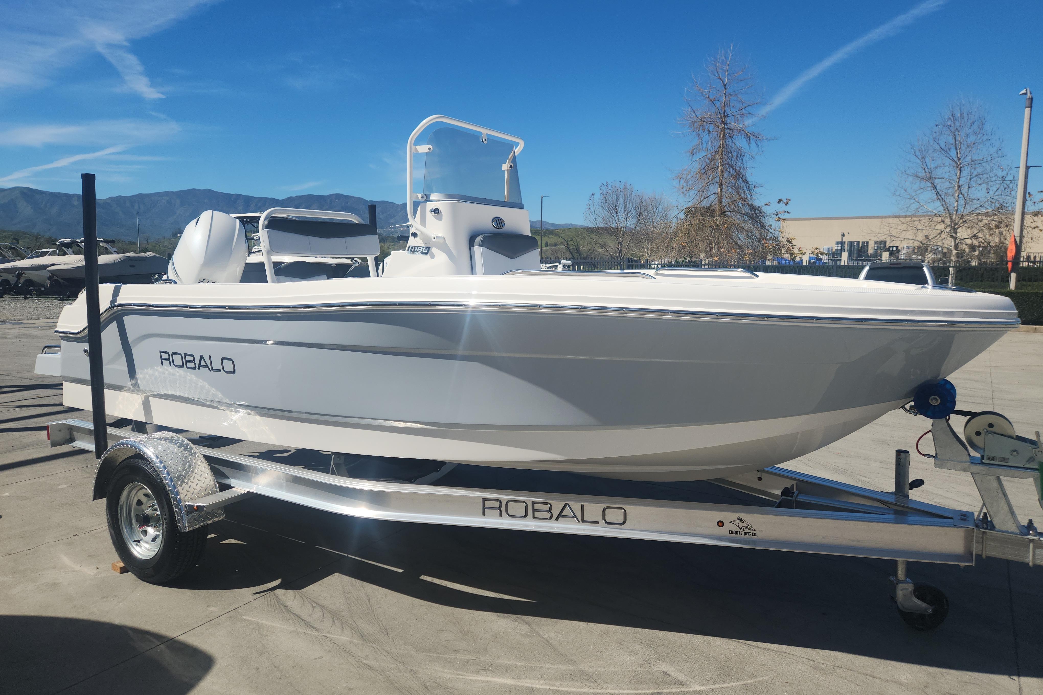 2026 Robalo R160 Center Console boat on trailer, parked outdoors under clear blue sky.