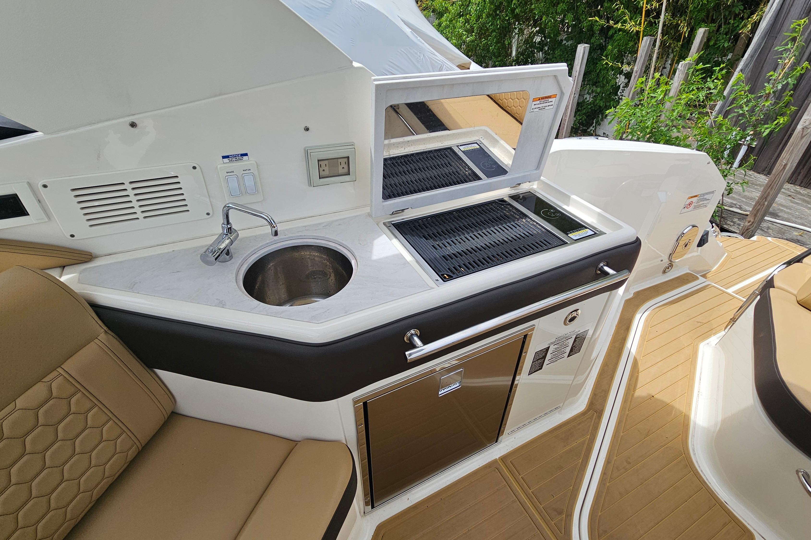 Luxurious 2023 Sea Ray Sundancer 320 yacht kitchenette with sink, grill, and seating area.